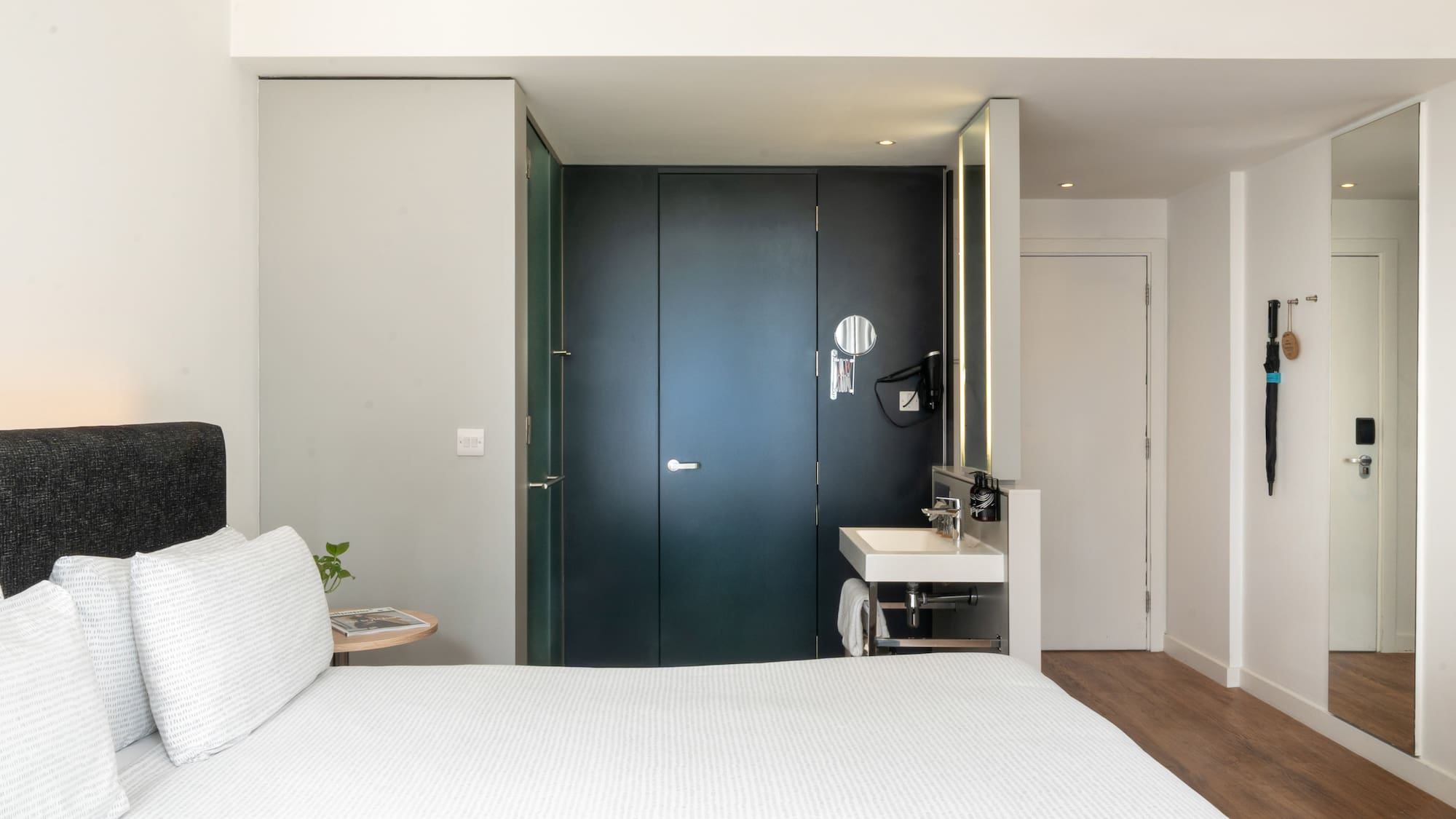 Minimalist hotel room with white bed, integrated vanity, and dark modern doors.
