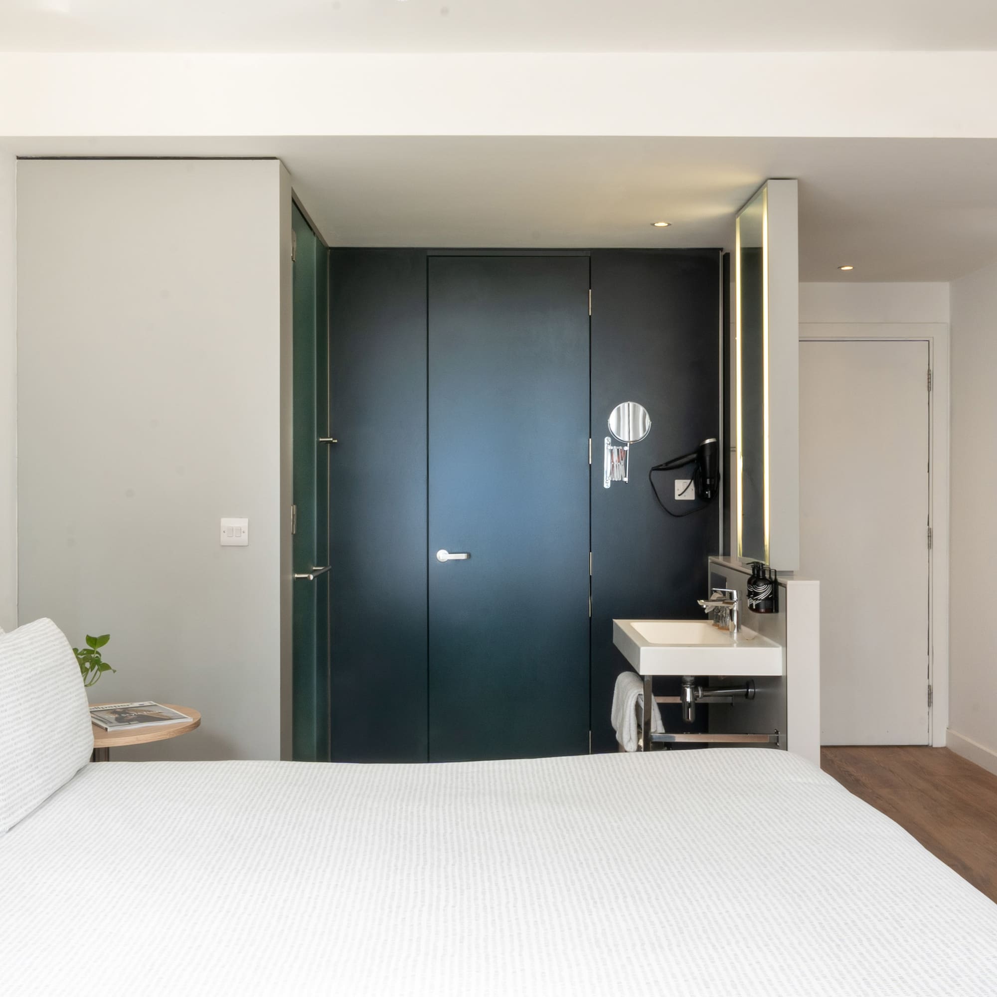 Minimalist hotel room with white bed, integrated vanity, and dark modern doors.