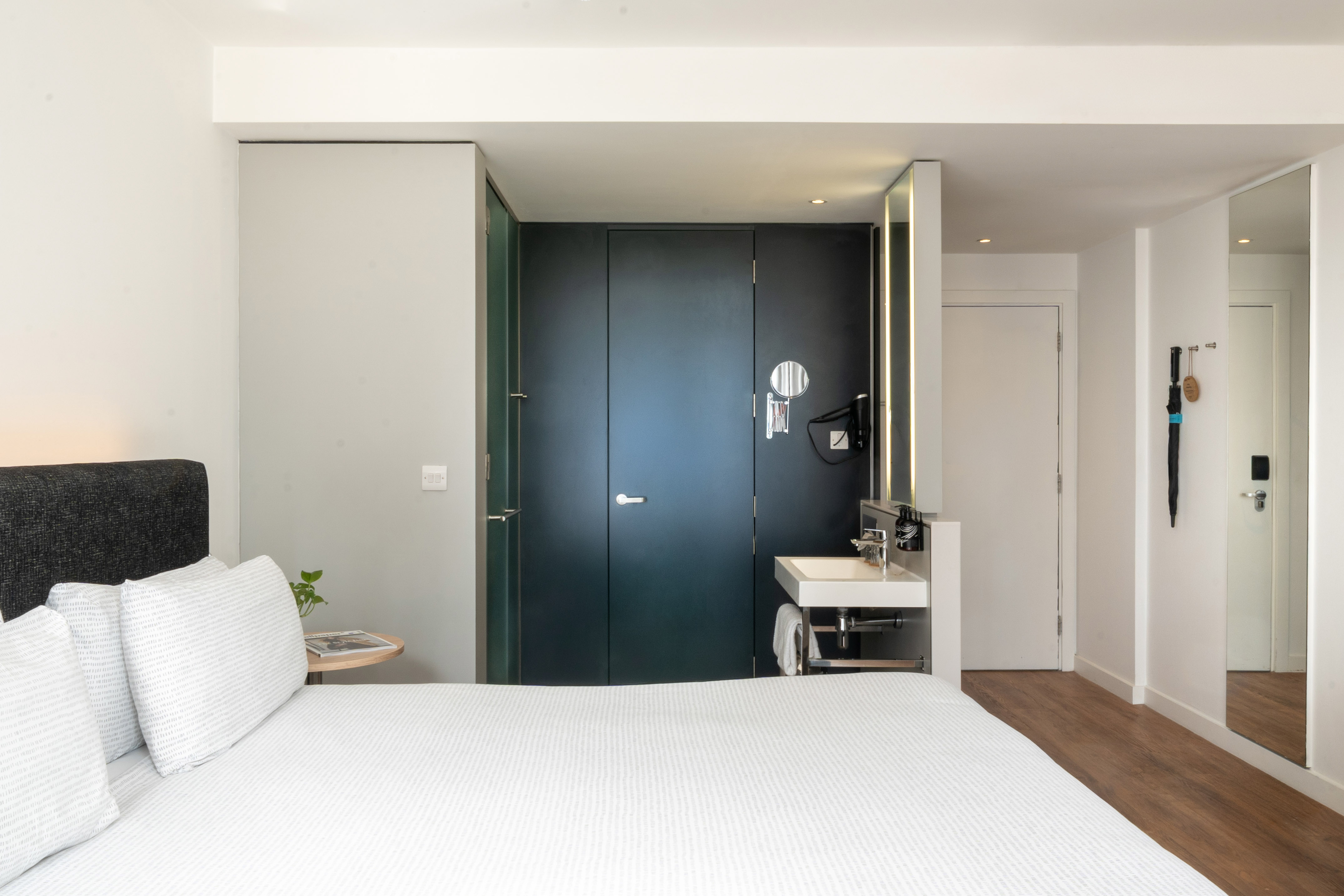 Minimalist hotel room with white bed, integrated vanity, and dark modern doors.
