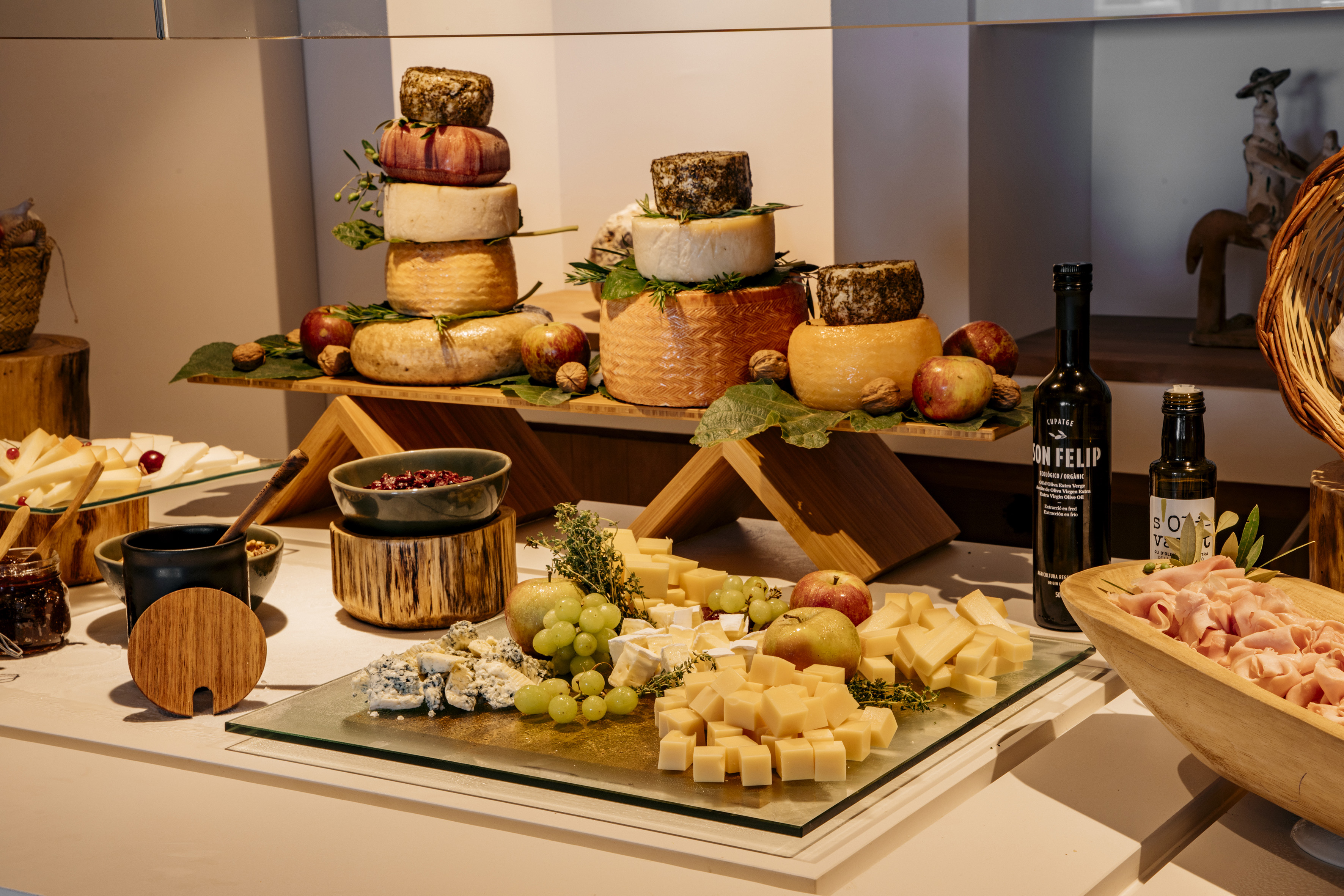 Cheese buffet display with stacked wheels, cut cheese, grapes, apples, and ham.