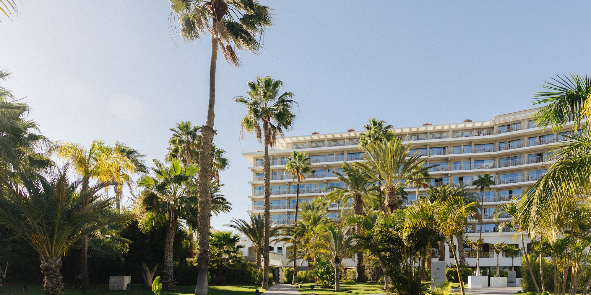 Sunny resort hotel with palm trees, green lawns, and a paved pathway.