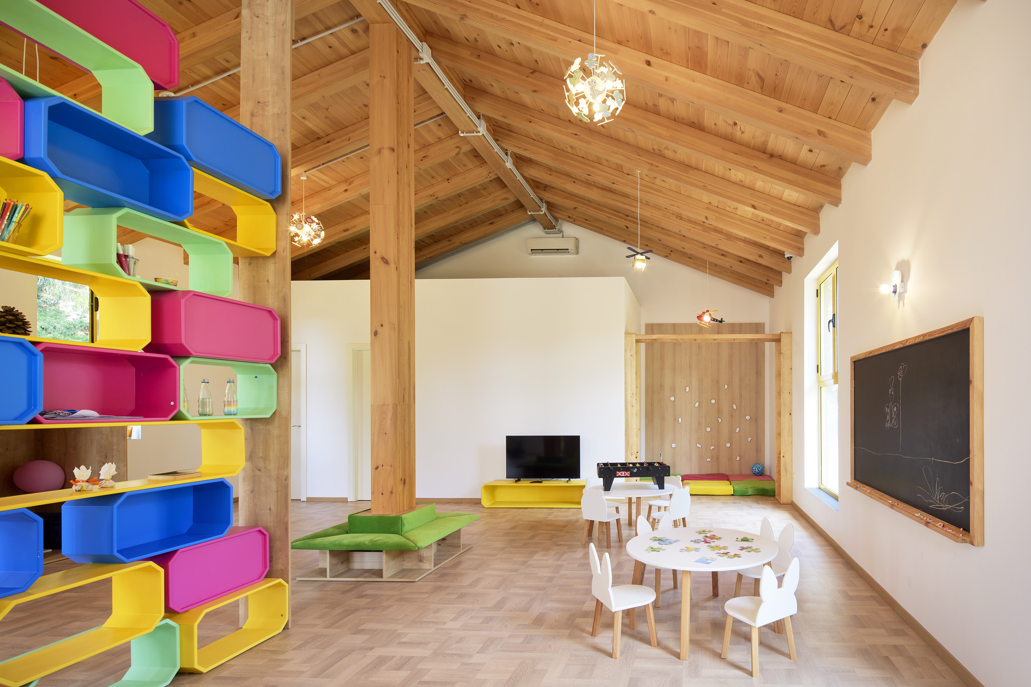 Bright children's play area with colorful shelves, wooden ceiling, and play tables.