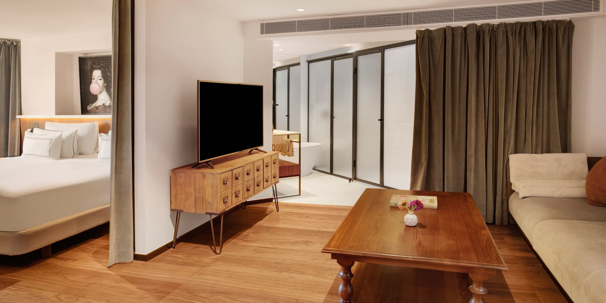 Modern hotel suite with integrated bedroom, living area, TV, and wood floor.
