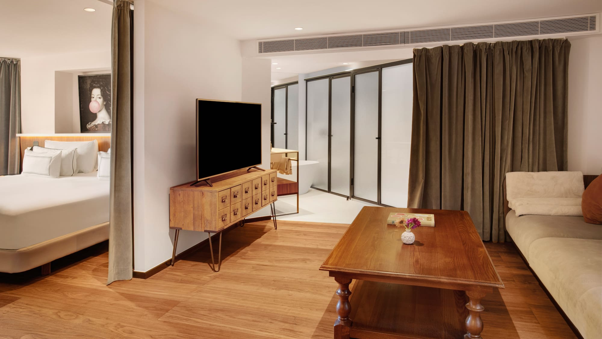 Modern hotel suite with integrated bedroom, living area, TV, and wood floor.