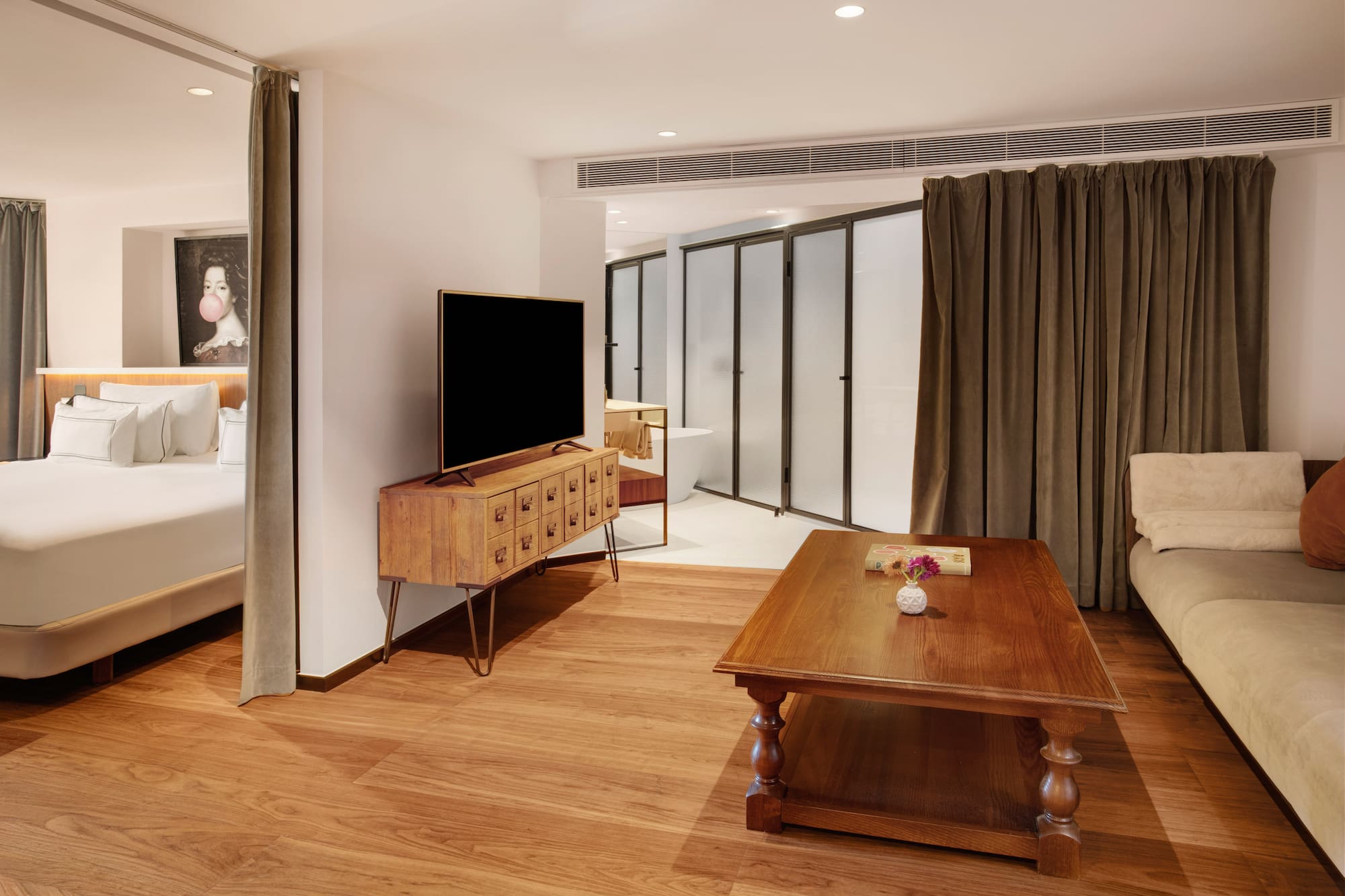 Modern hotel suite with integrated bedroom, living area, TV, and wood floor.