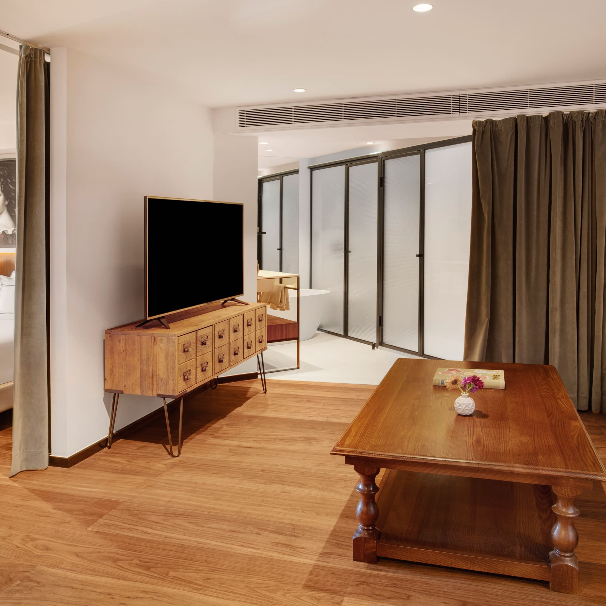 Modern hotel suite with integrated bedroom, living area, TV, and wood floor.