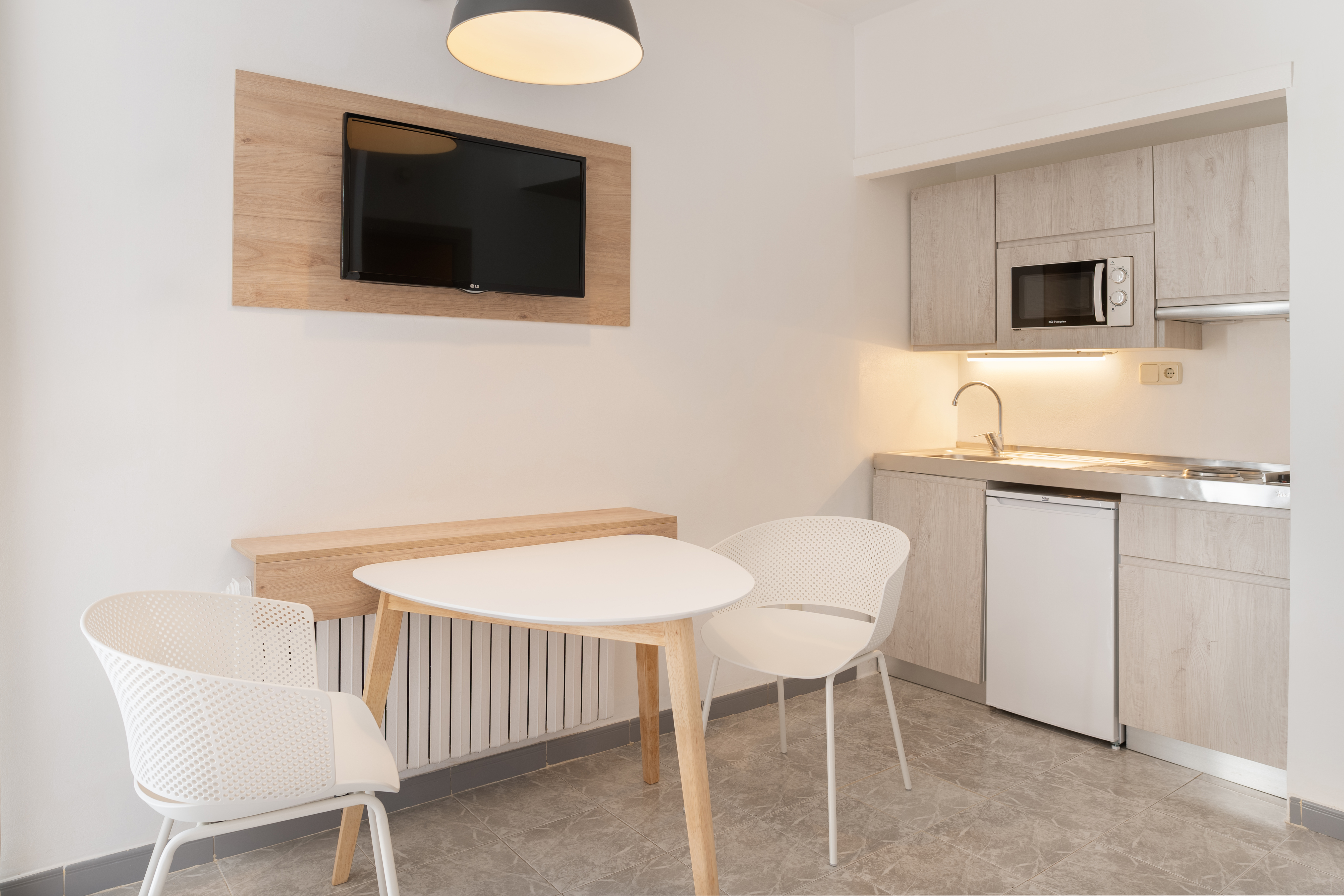 Modern studio apartment with kitchenette, wall-mounted TV, and dining area with two chairs.