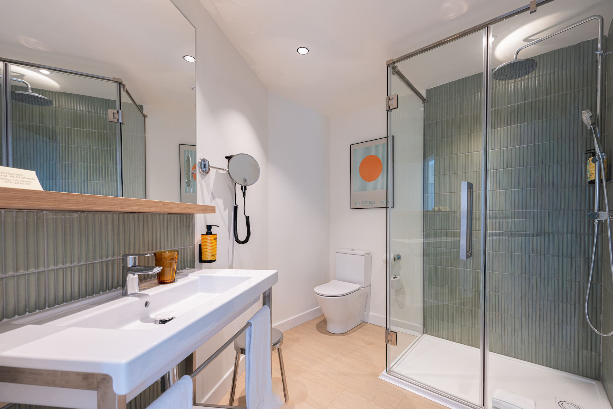Modern bathroom with glass shower, white sink, toilet, and stylish green tile walls.