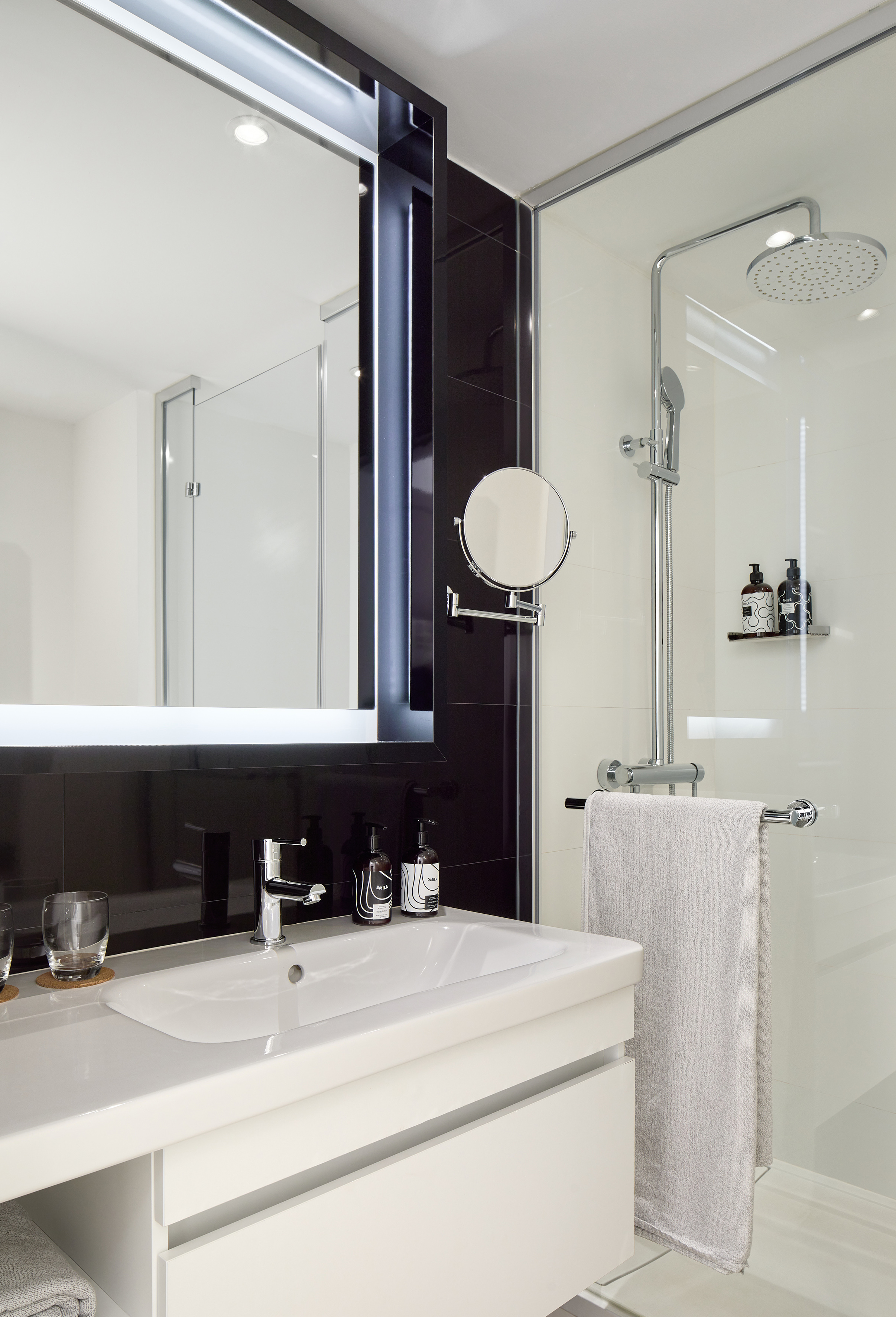 Modern black and white bathroom with vanity, lighted mirror, glass shower.