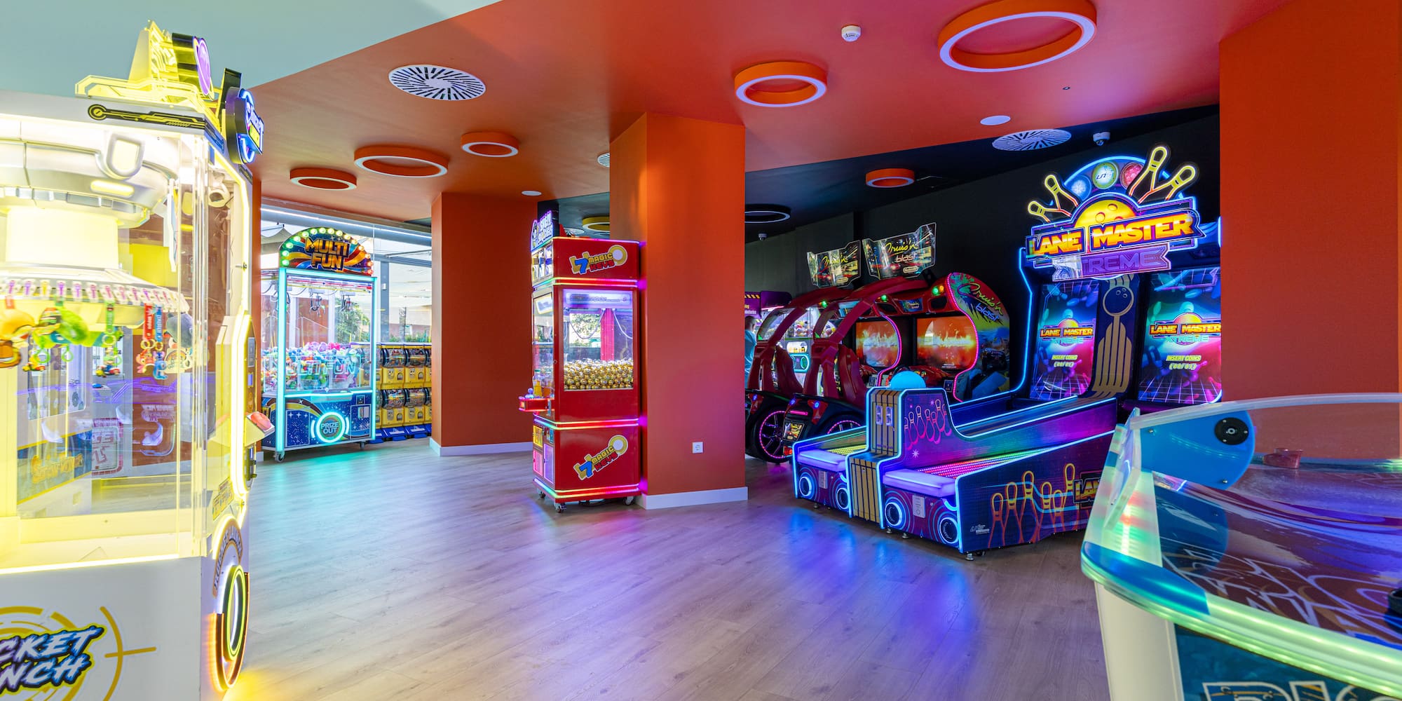 Neon-lit arcade room with claw machines, bowling, and racing game cabinets.