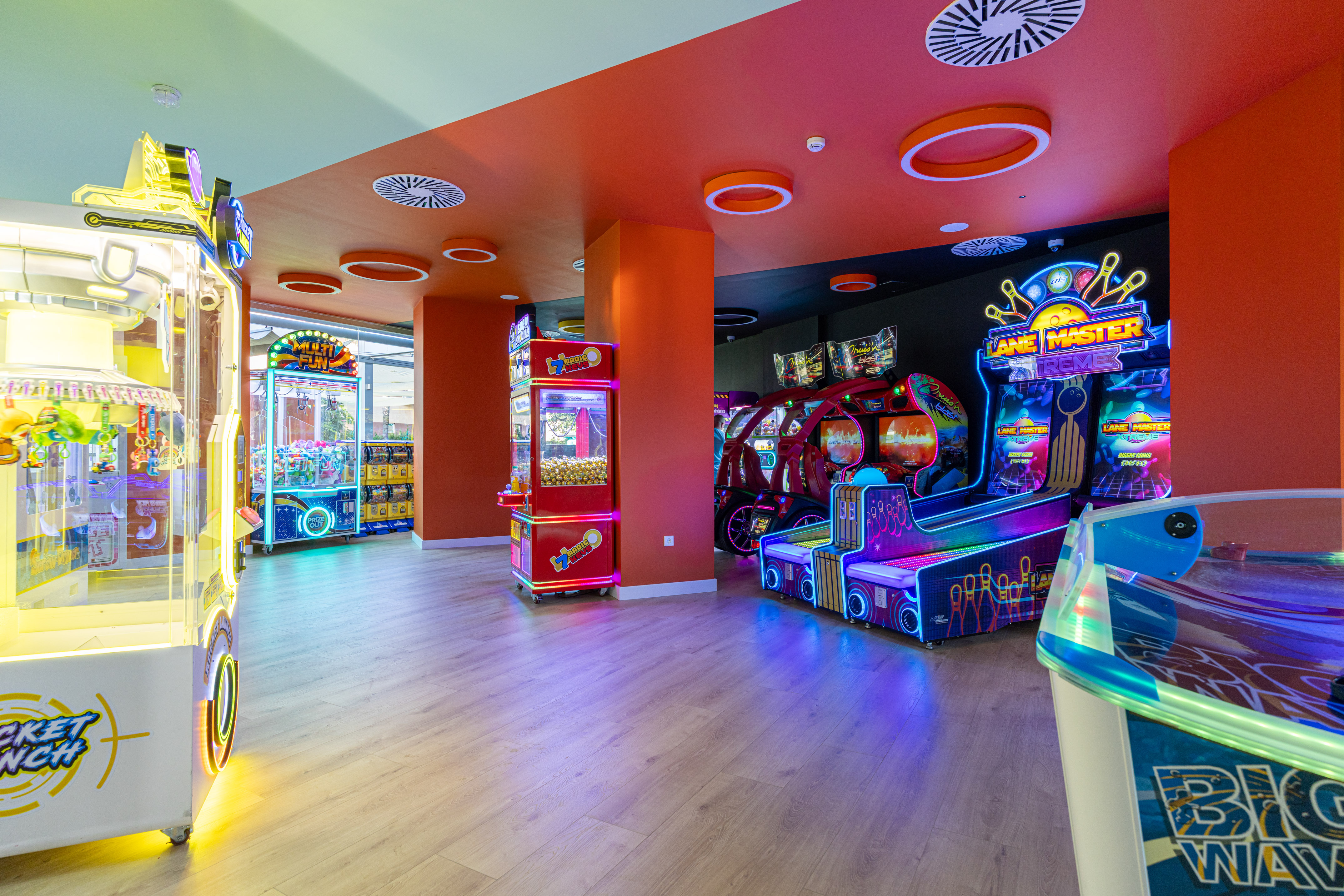 Neon-lit arcade room with claw machines, bowling, and racing game cabinets.