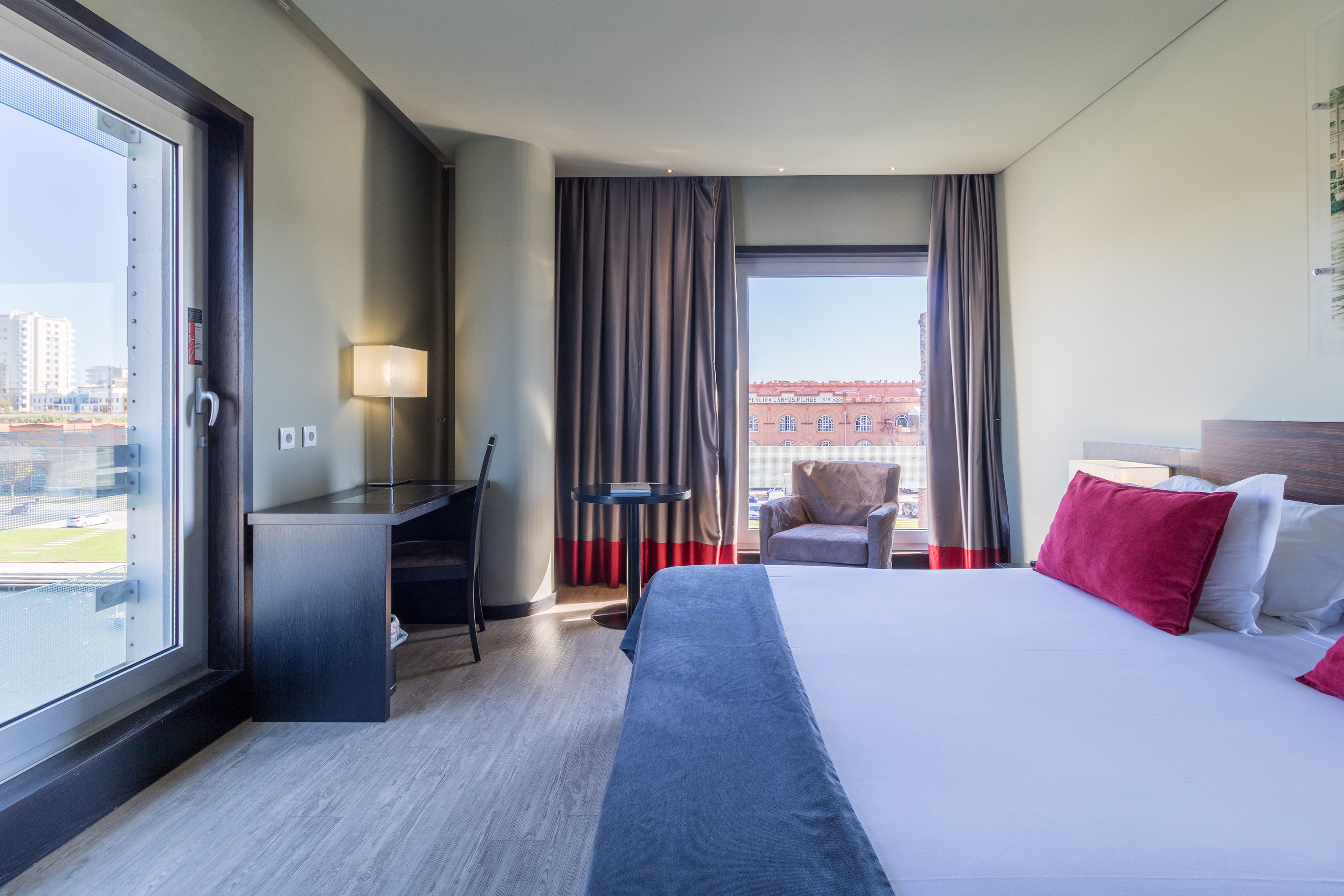 Modern hotel room with bed, work desk, and large window offering a city view.