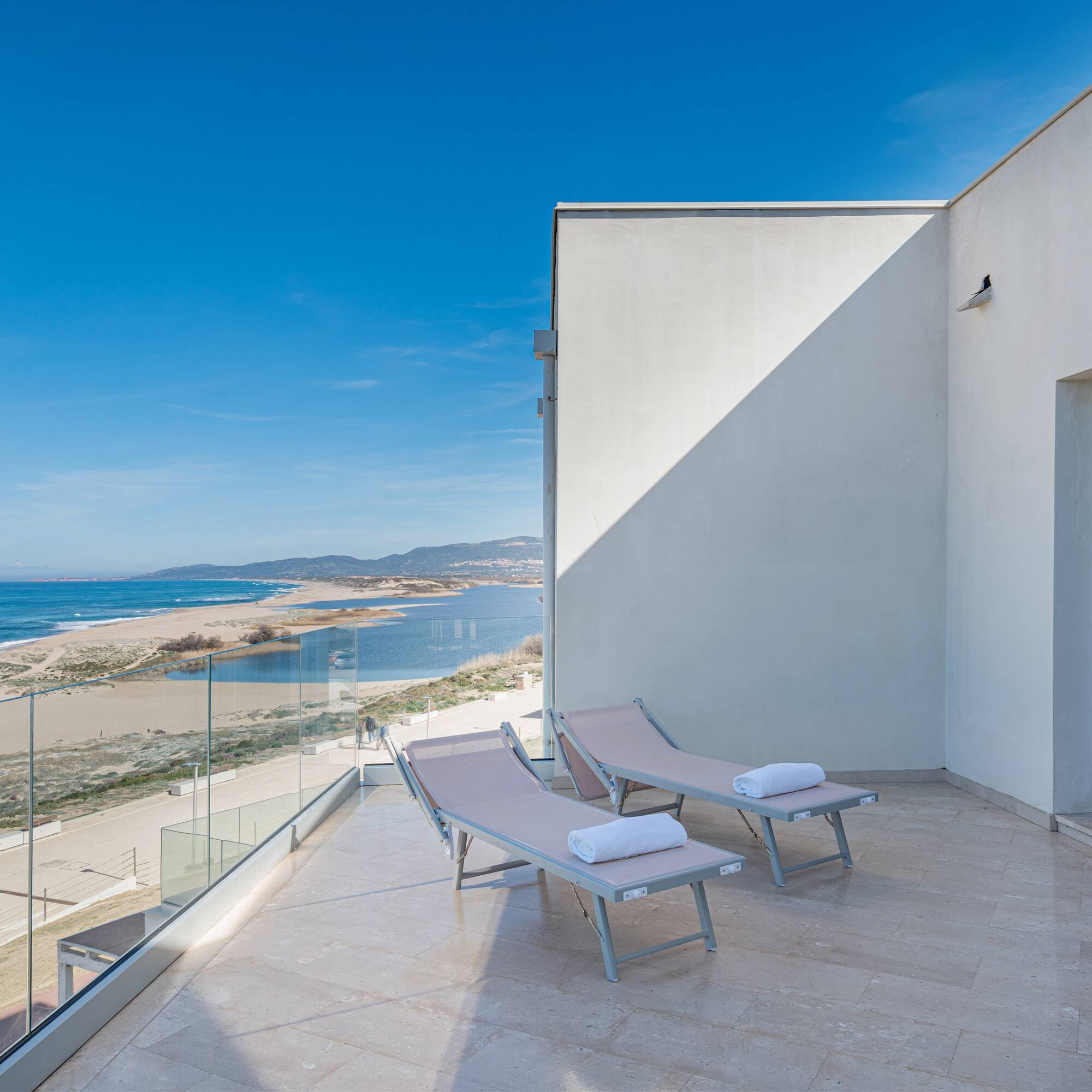 a deck with chairs and towels on a balcony overlooking a beach