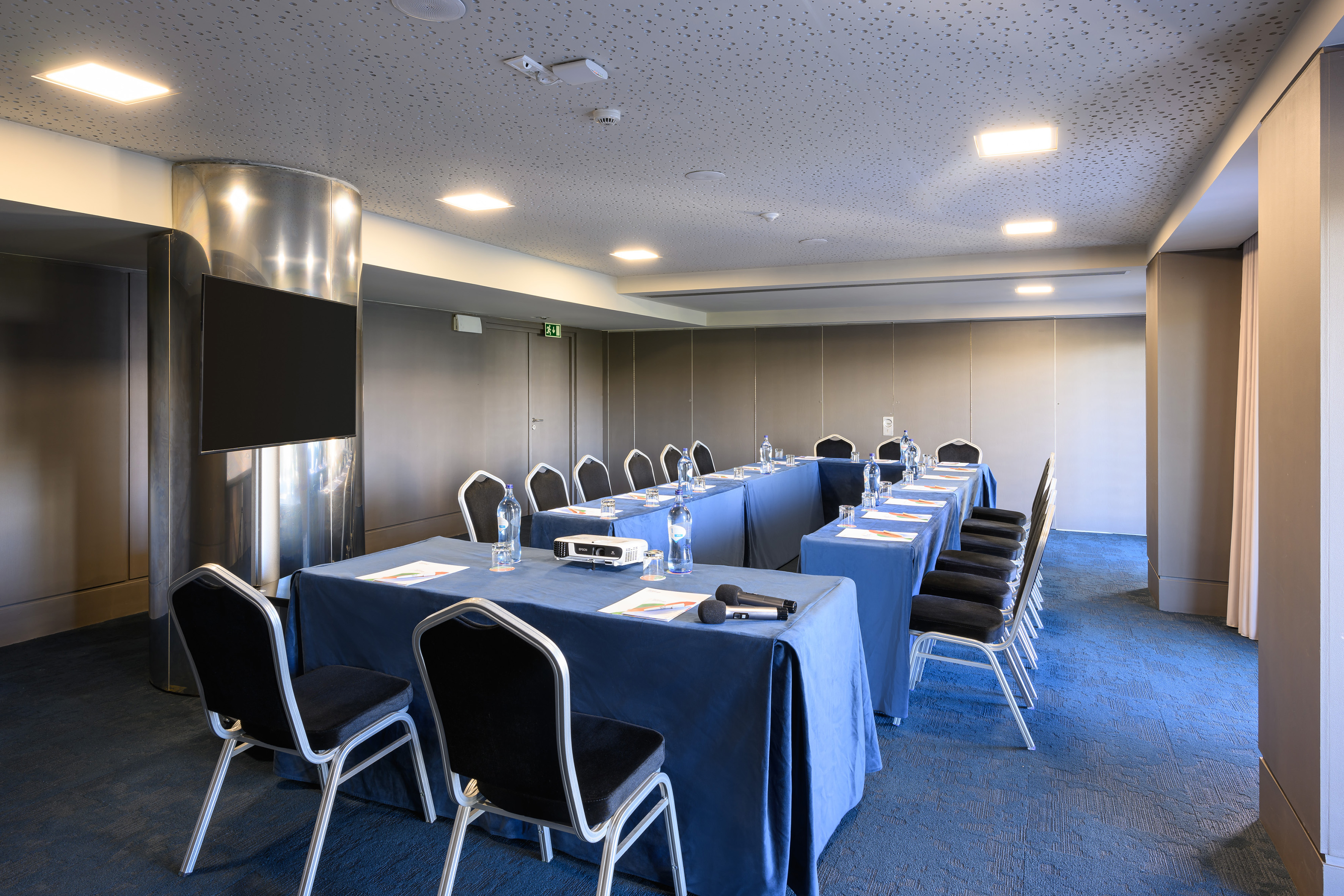 U-shape conference room with blue tables, black chairs, and presentation screen.