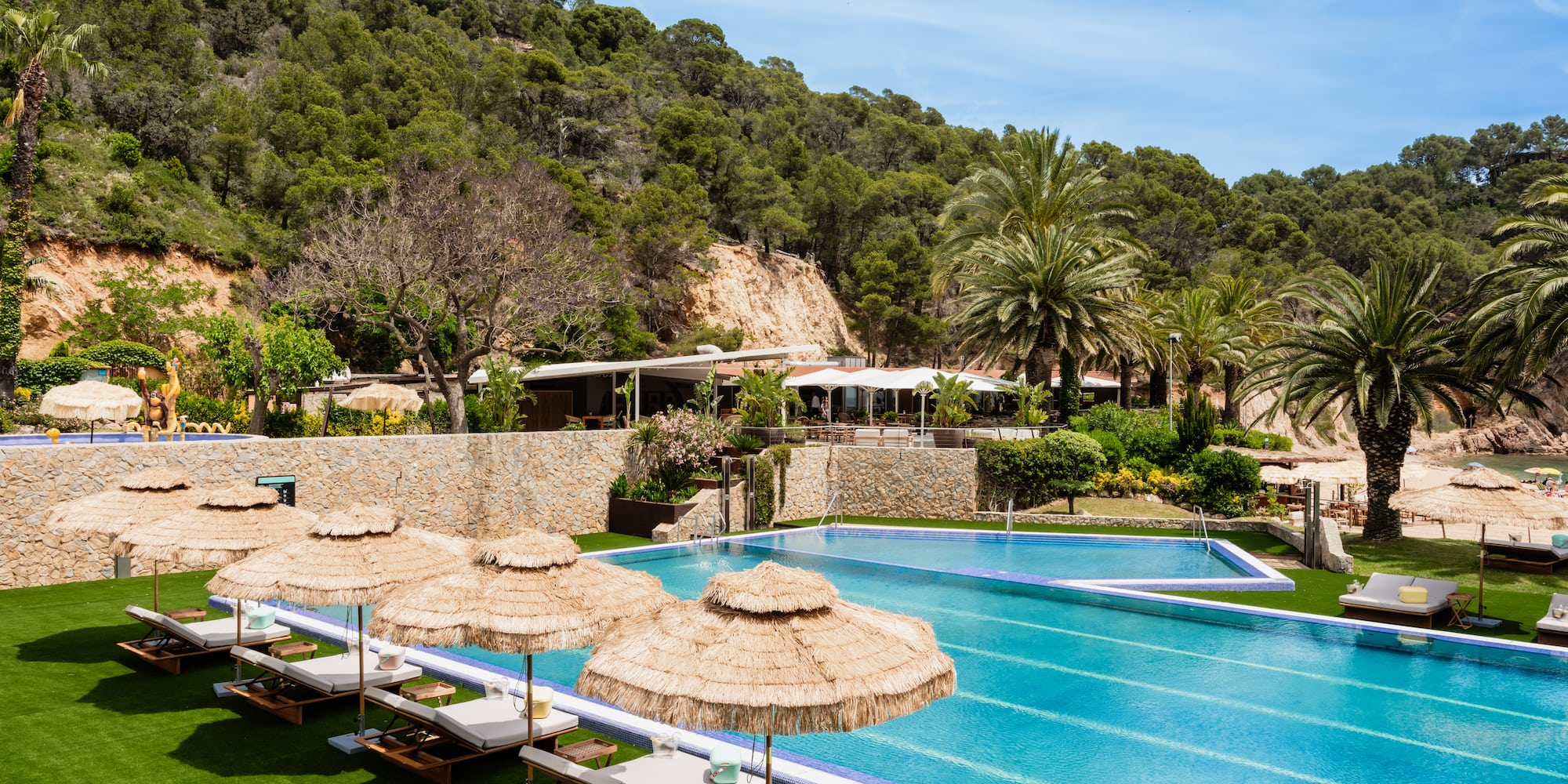 a pool with umbrellas and chairs in front of a hill