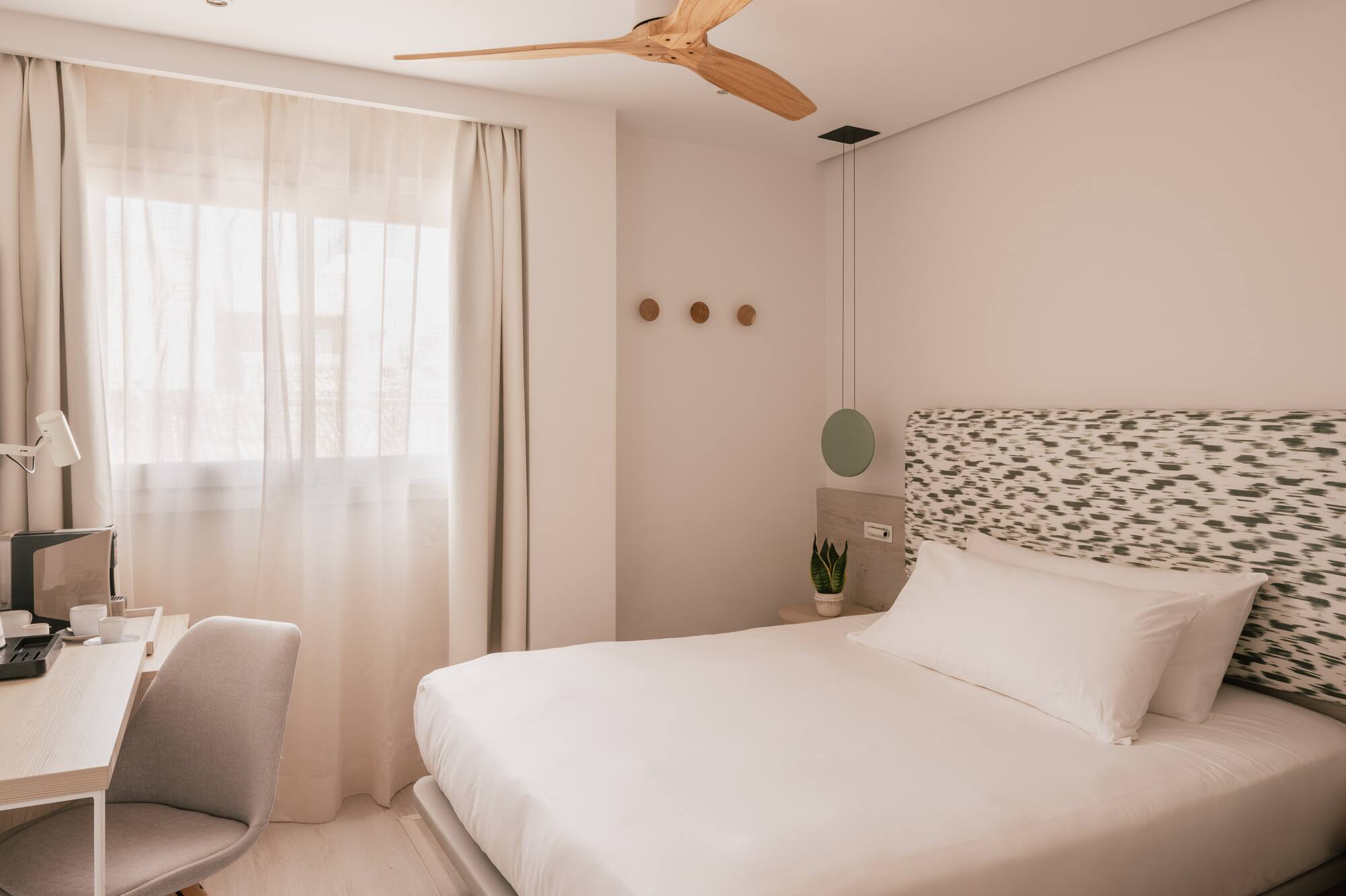 Habitación hotel moderna con cama, escritorio, ventana y ventilador de techo.