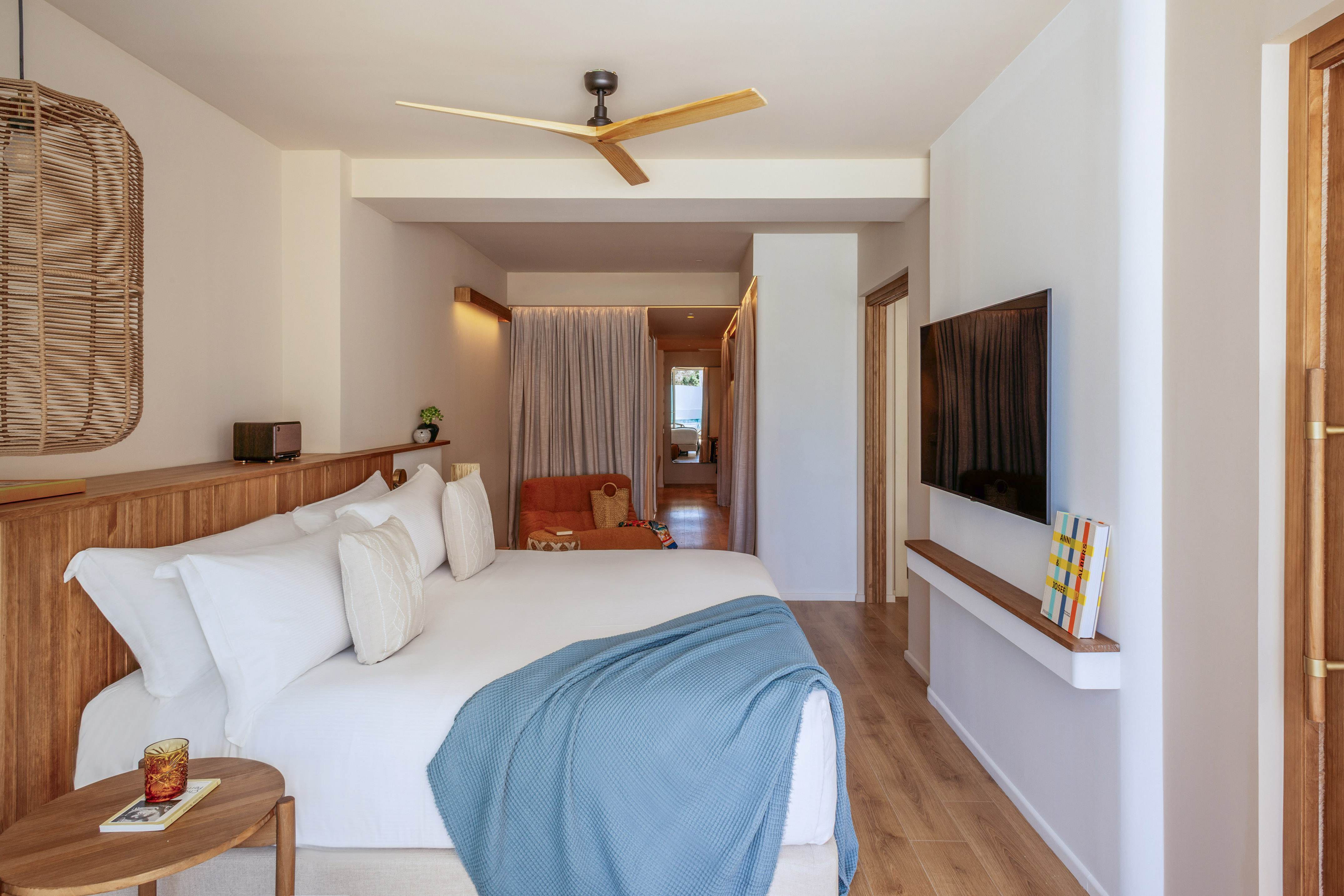 Bright hotel bedroom with wooden bed, blue throw blanket, and ceiling fan.