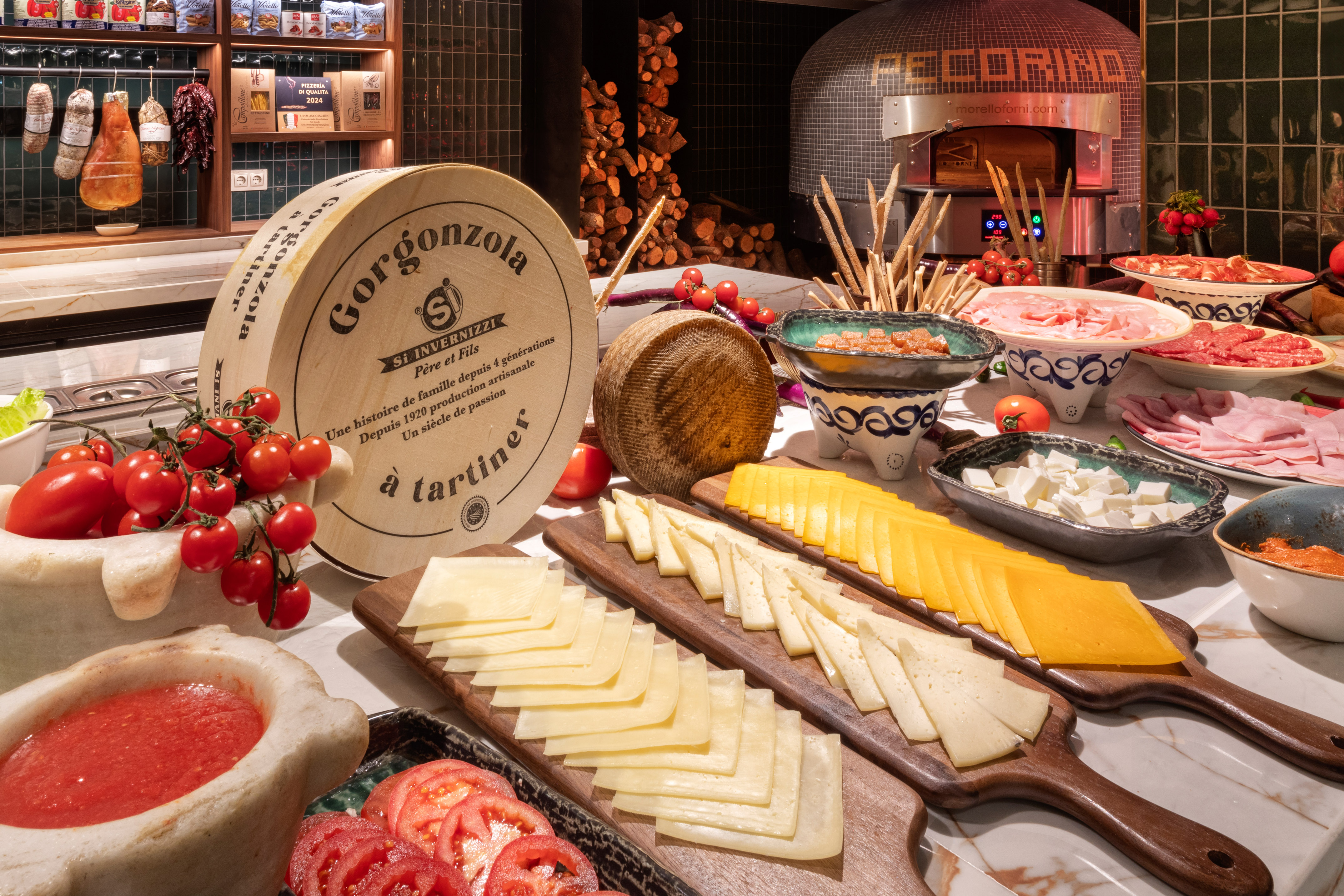 Gorgonzola wheel, sliced cheeses, cured meats, fresh tomatoes, and pizza oven.
