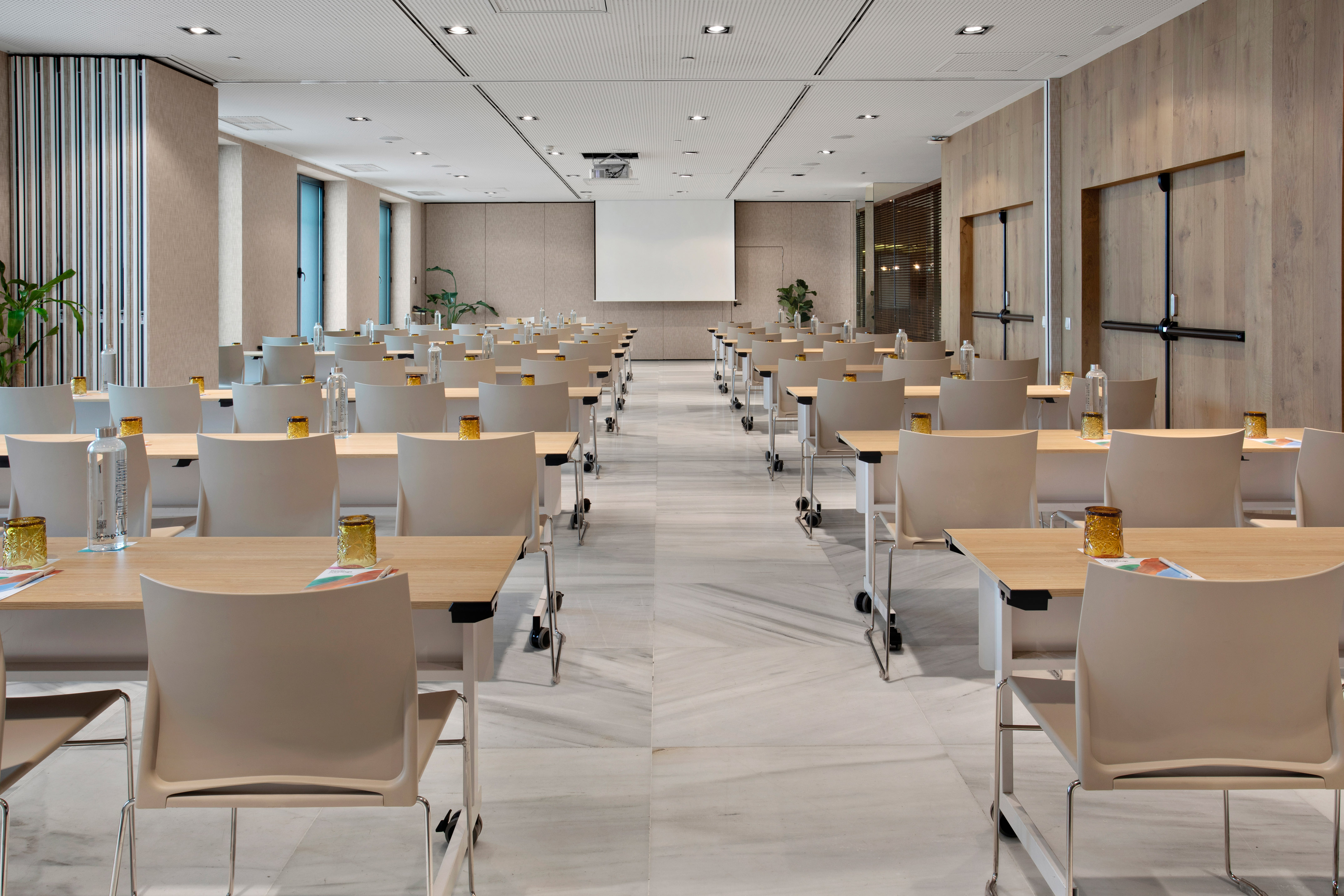 Modern empty conference room with rows of tables, chairs, and projector screen.