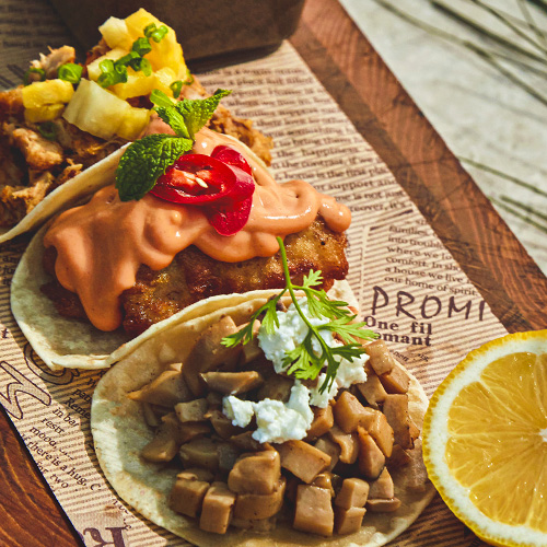 Gourmet tacos with pineapple, spicy sauce, crumbled cheese, and lemon.