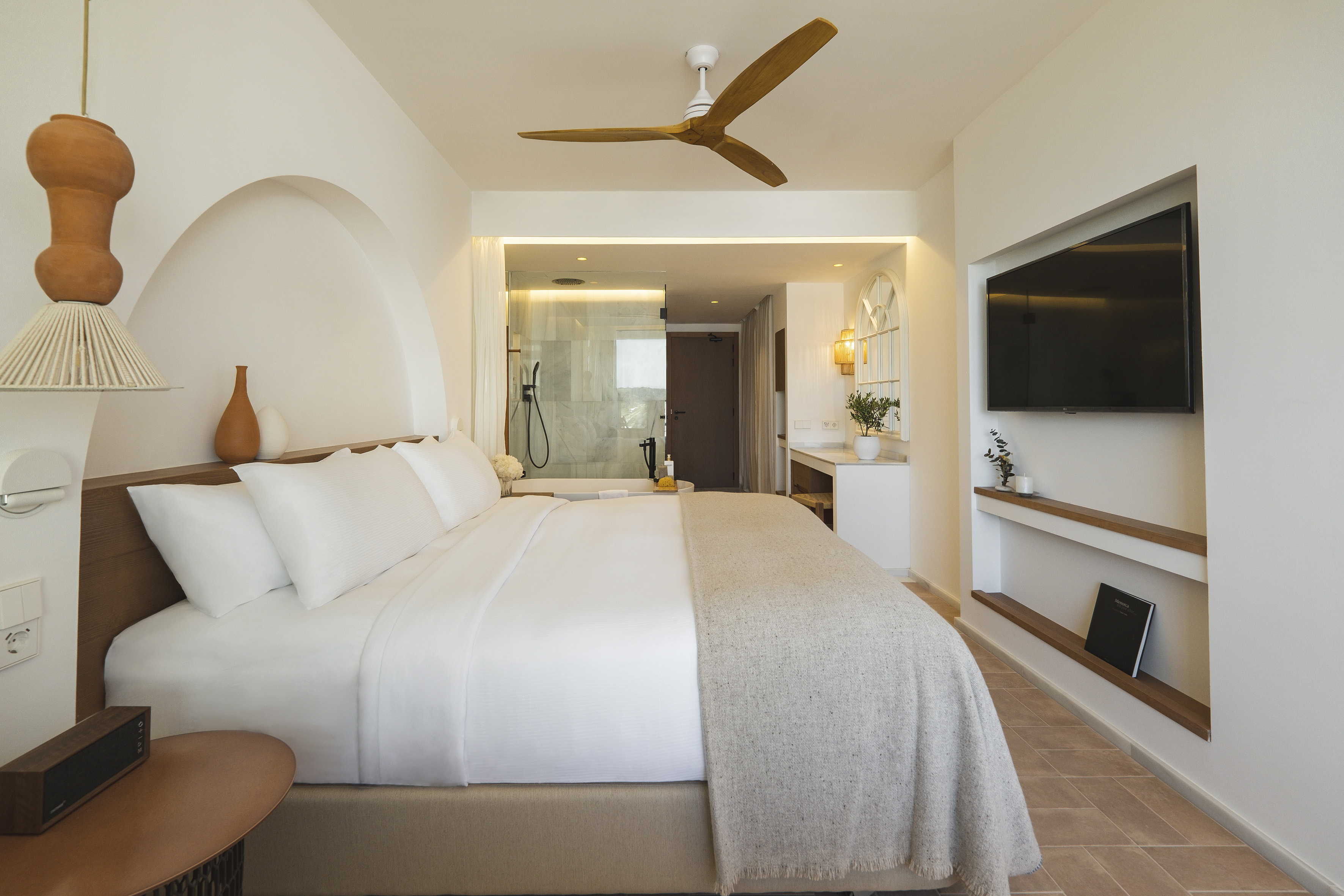 Luxury hotel bedroom with king bed, minimalist decor, and open shower.