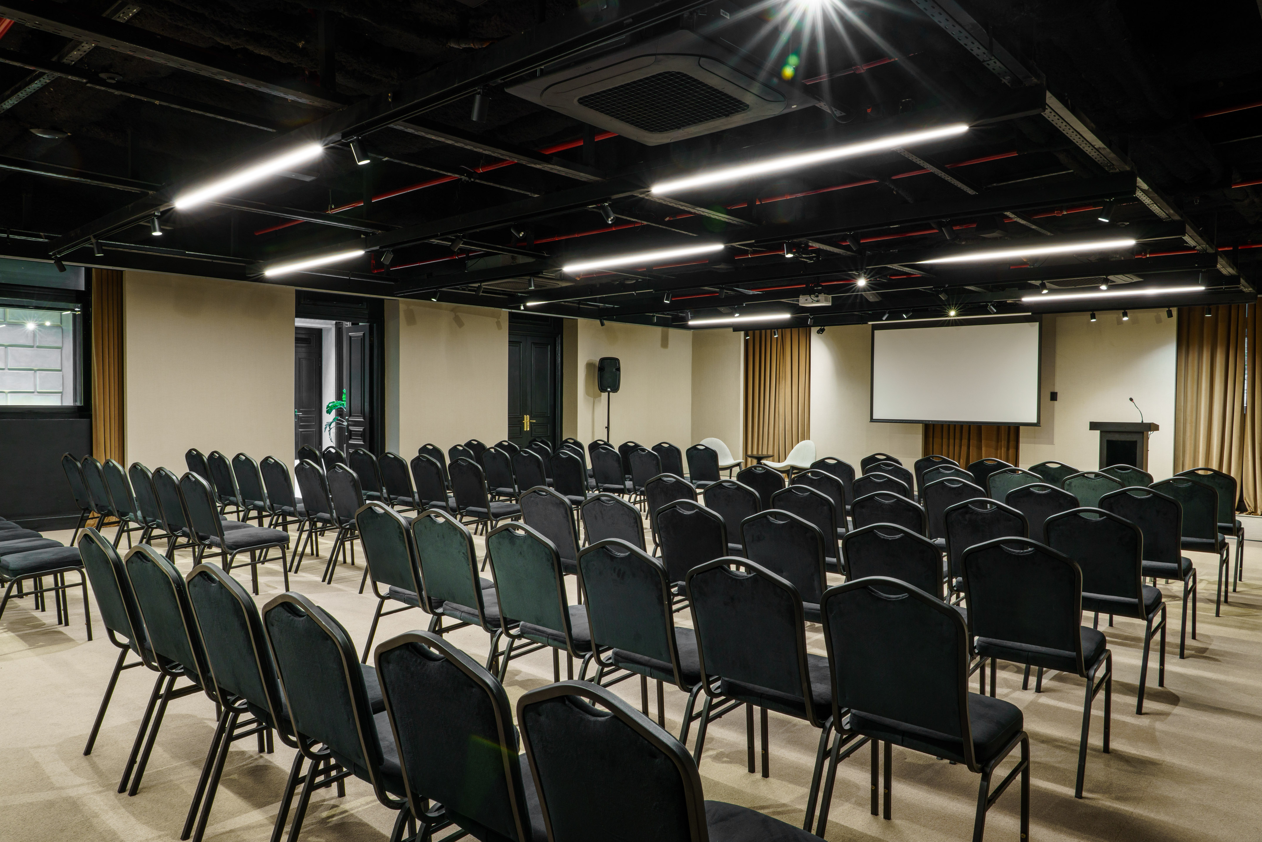 Modern presentation room with rows of black chairs, screen, and podium.