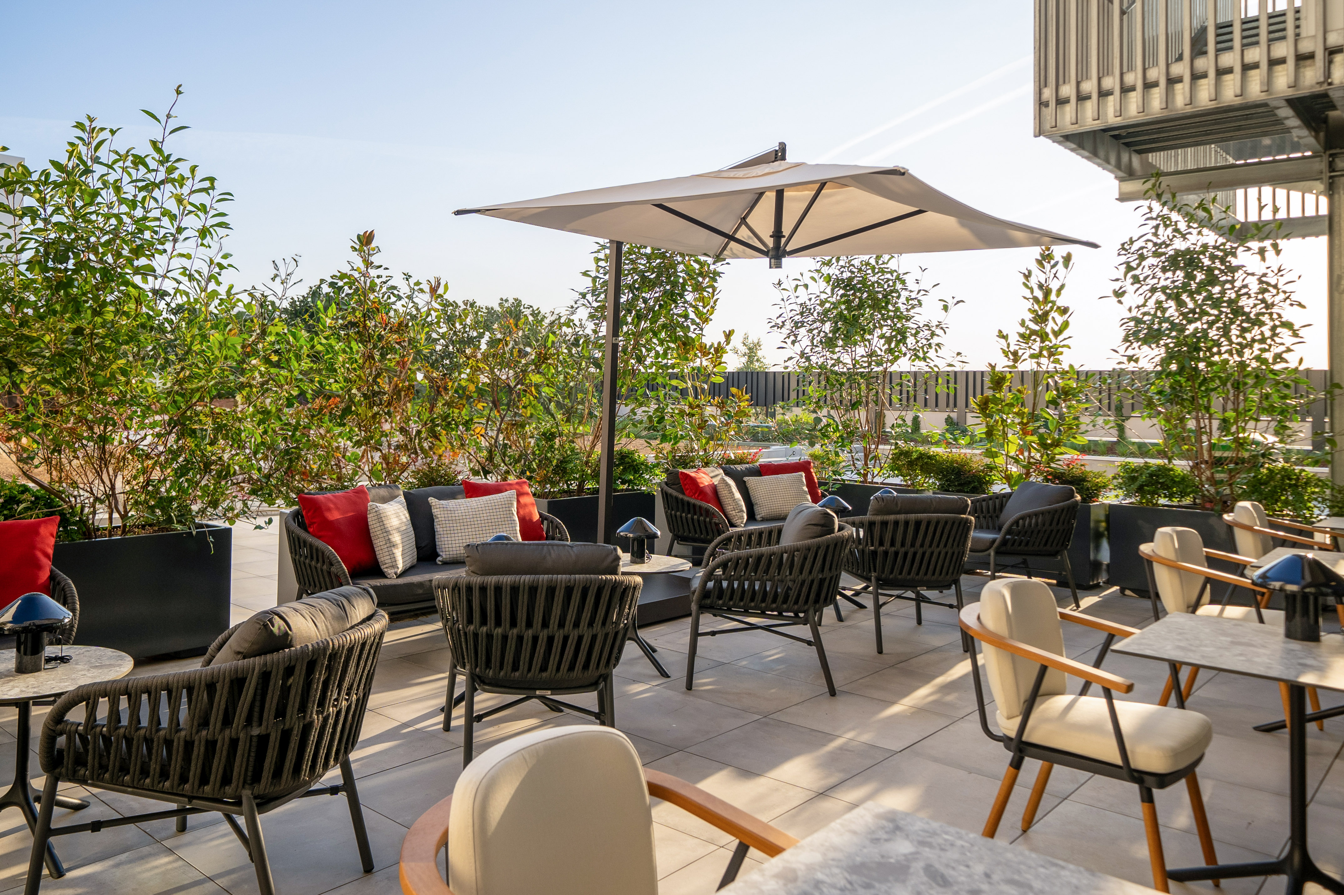 Hotel terrace lounge with modern outdoor seating, red pillows, and umbrella.