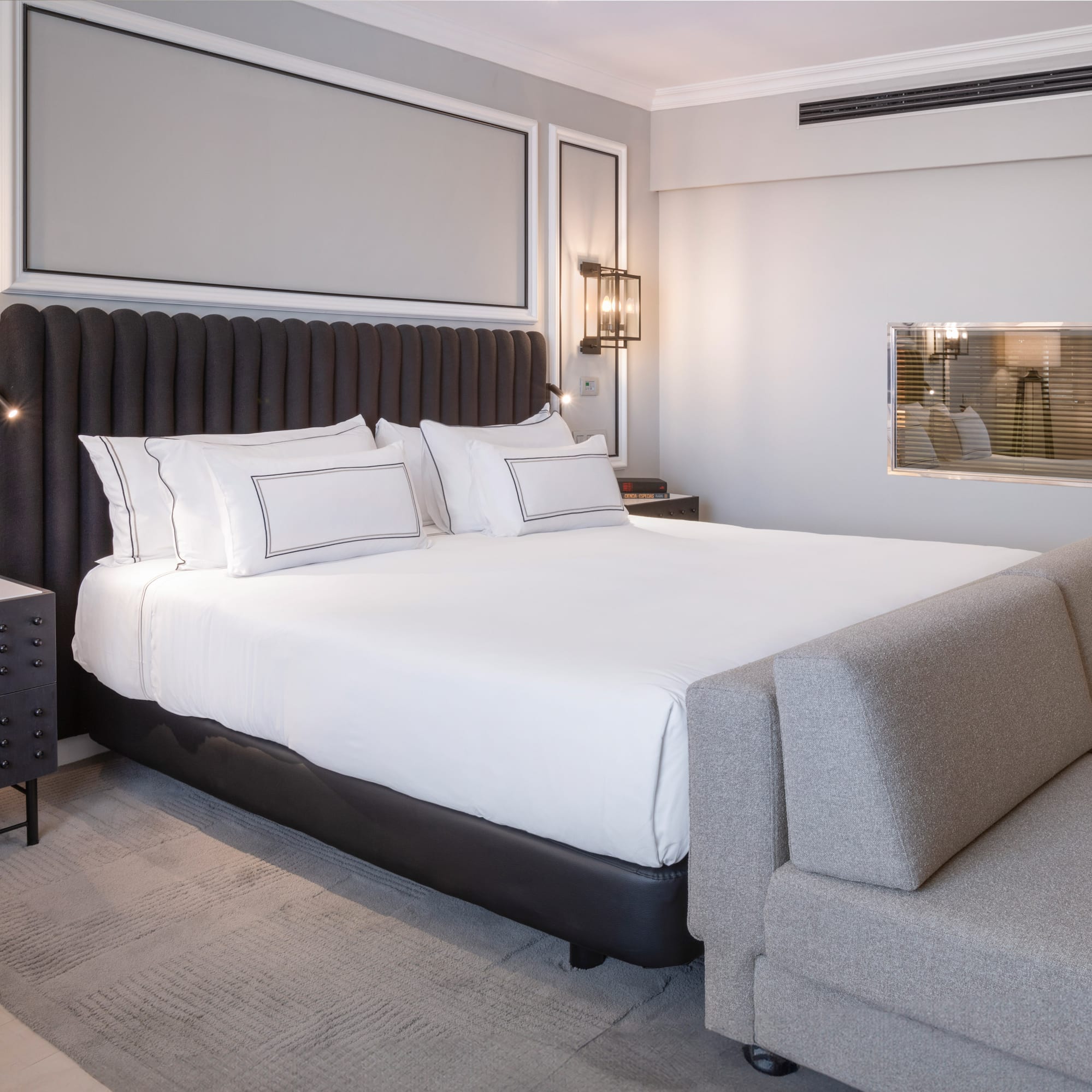 a bed with white sheets and a gray couch in a room