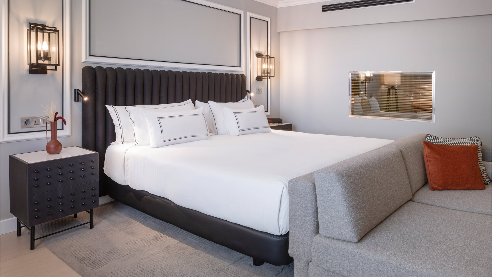 a bed with white sheets and a gray couch in a room