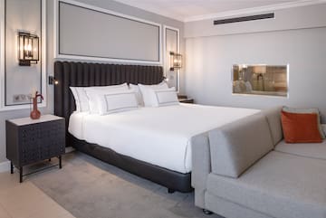 a bed with white sheets and a gray couch in a room