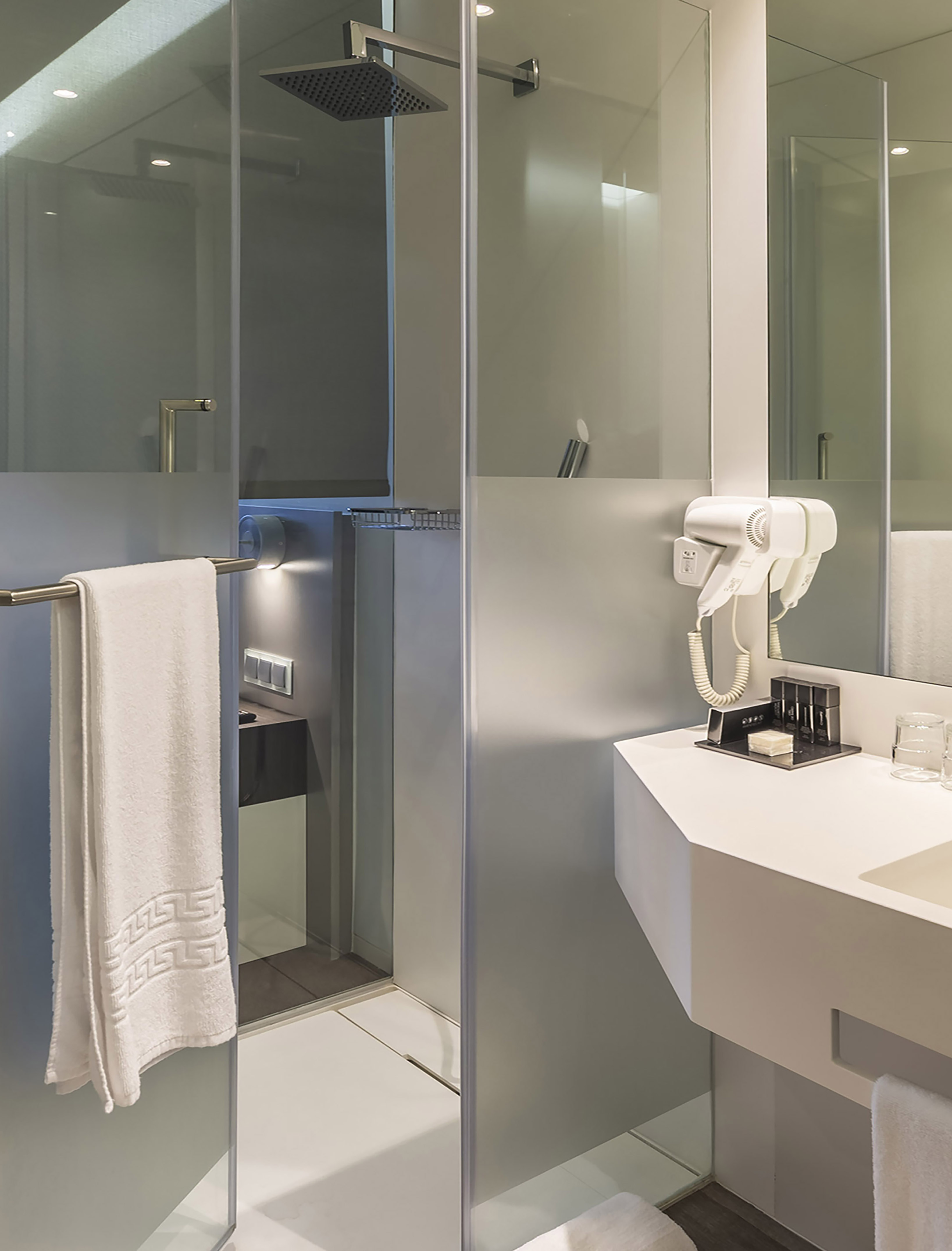 Sleek hotel bathroom with glass rain shower, white vanity, and hairdryer.