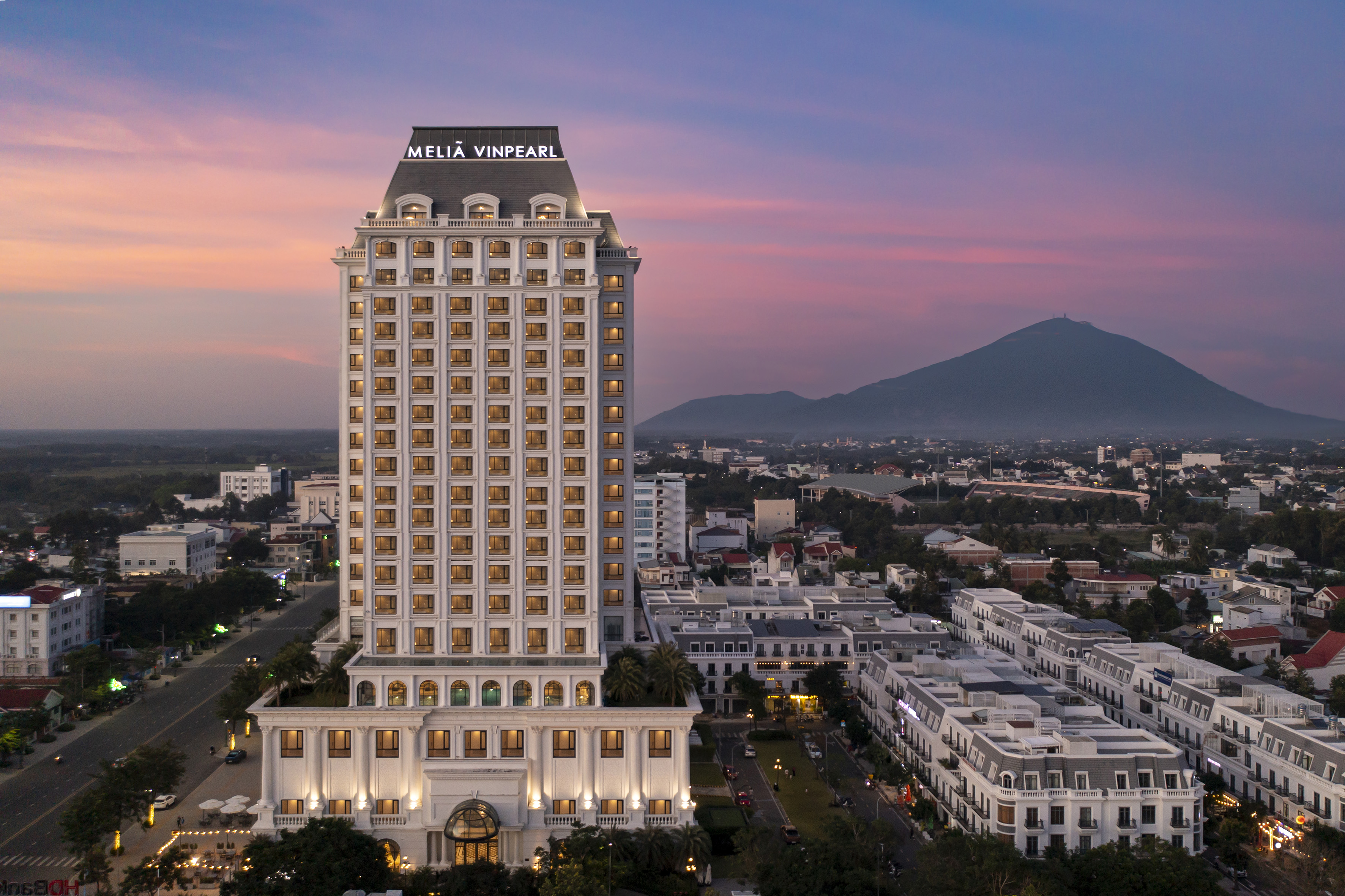 Melia Vinpearl hotel at dusk, city lights, mountain in background.