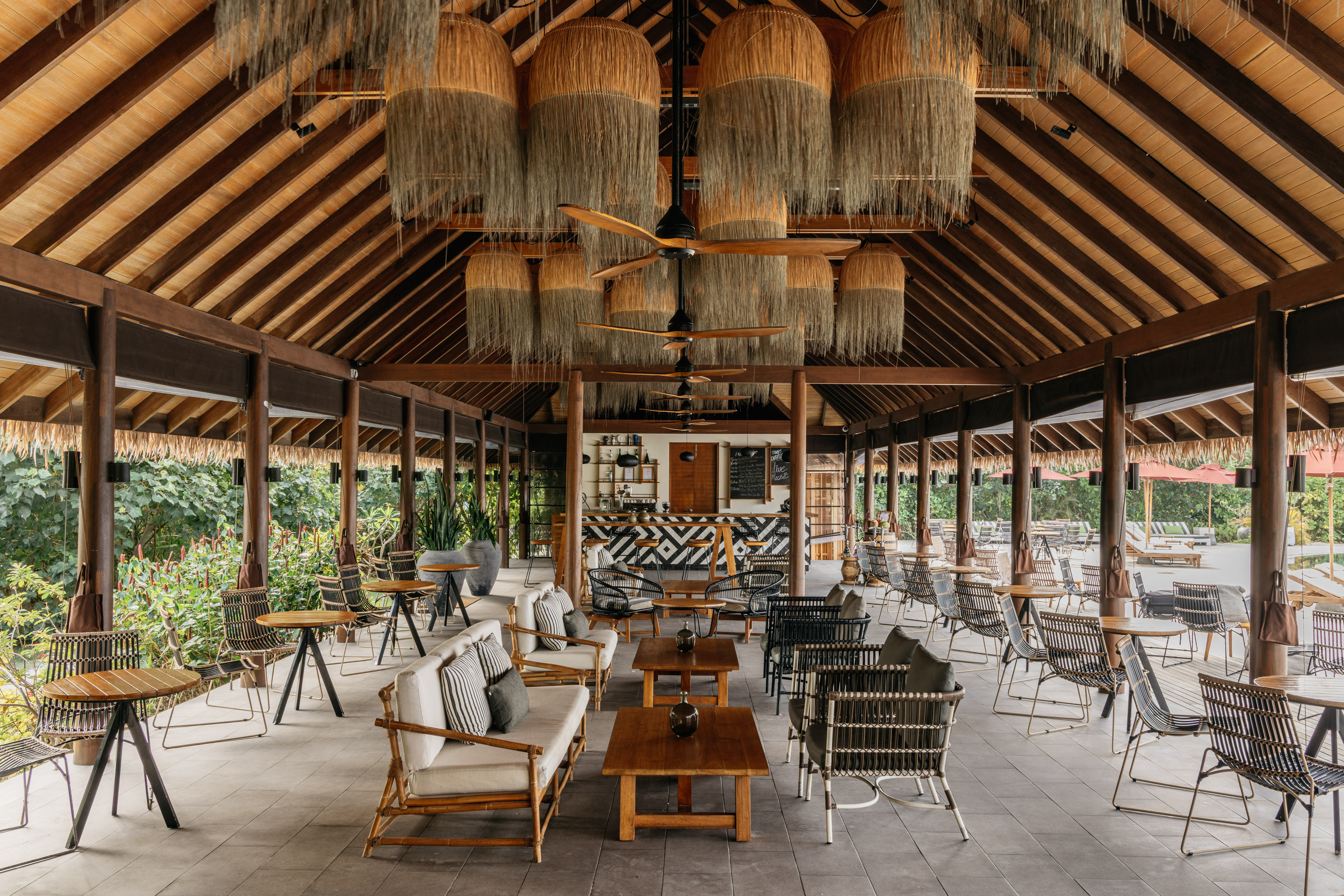 Tropical resort bar lounge: wooden ceiling, woven lights, natural seating.