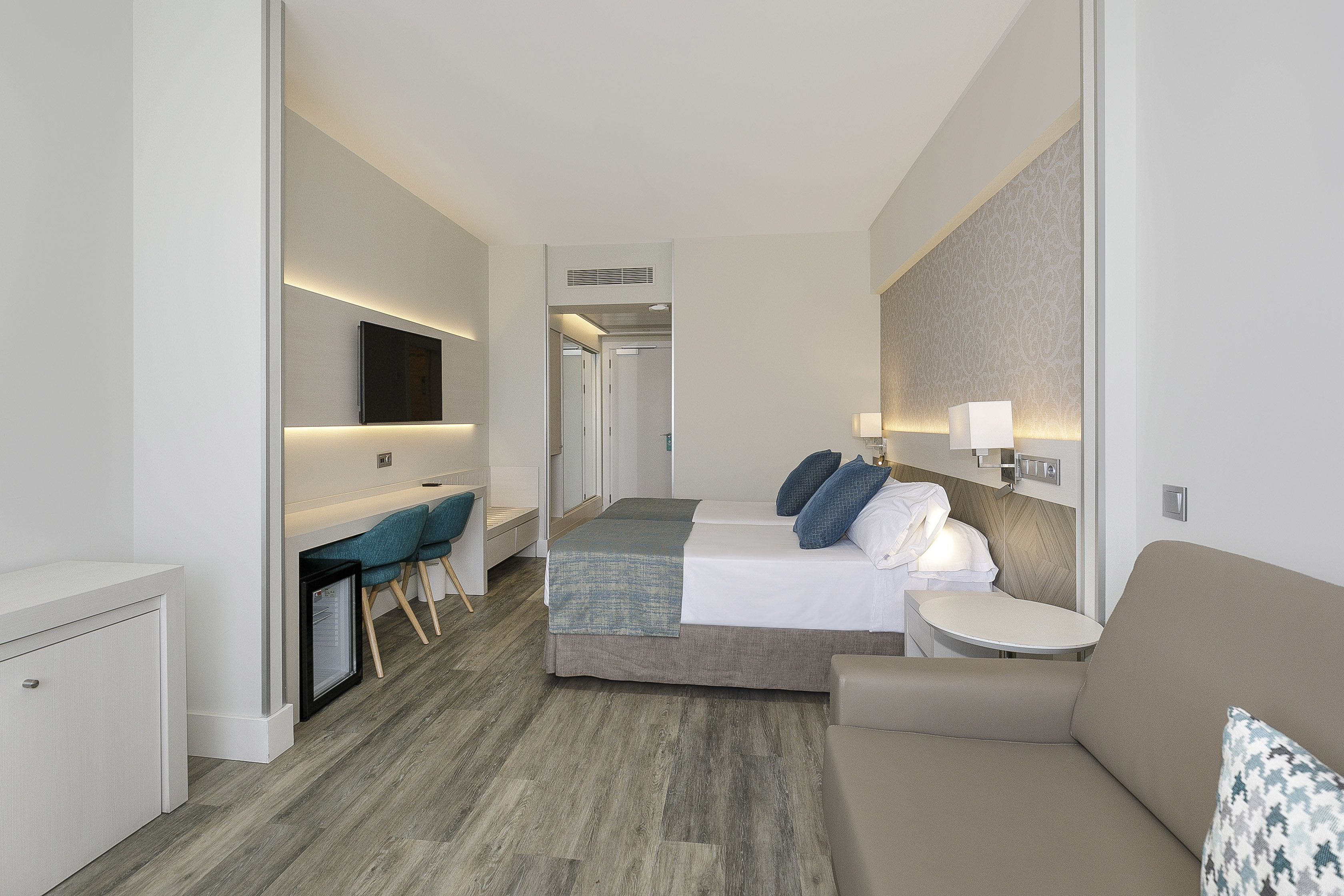 Modern hotel room with twin beds, work desk, TV, and comfortable seating.
