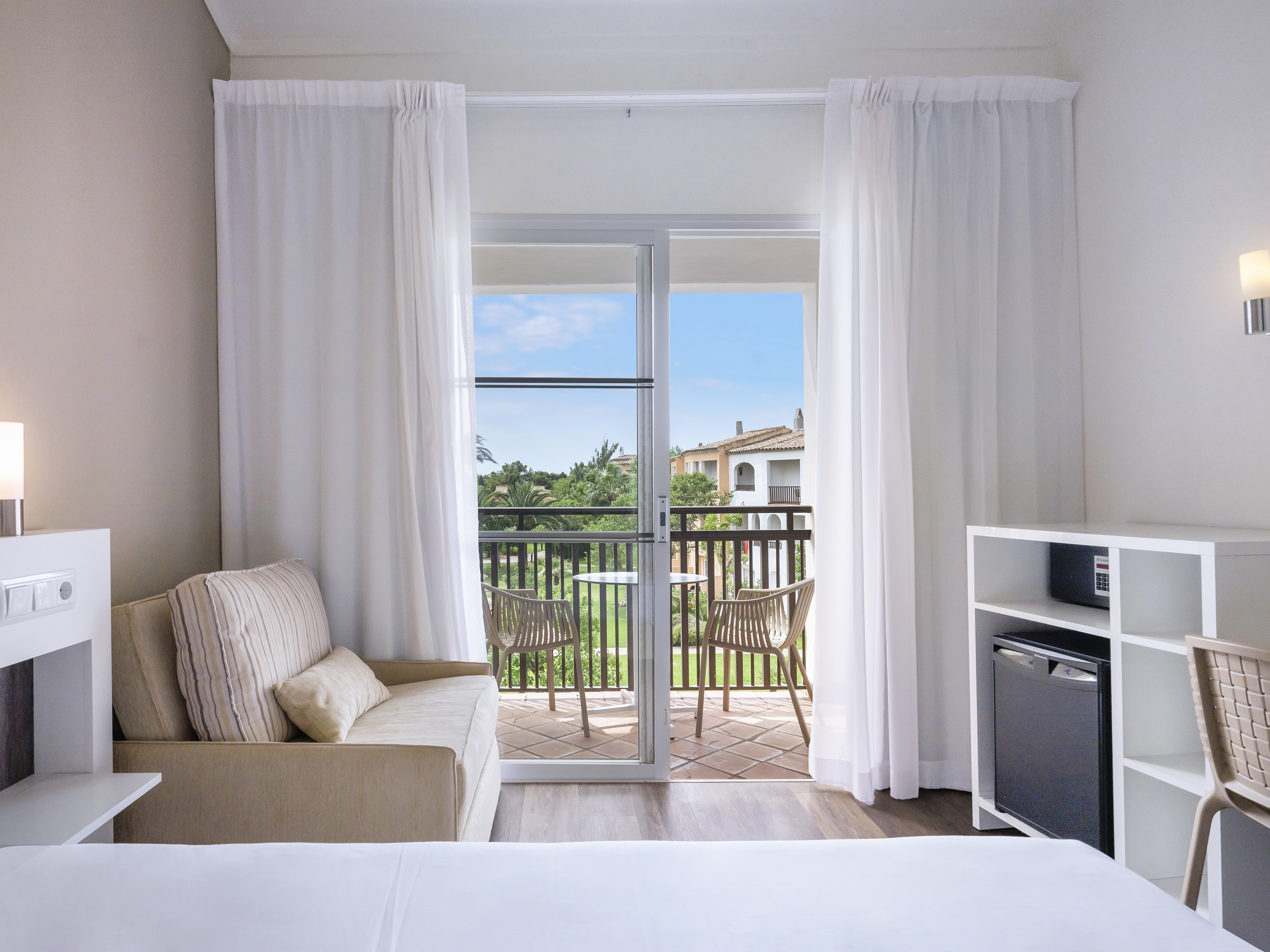 Hotel room with private balcony, daybed, mini-fridge, and resort view.