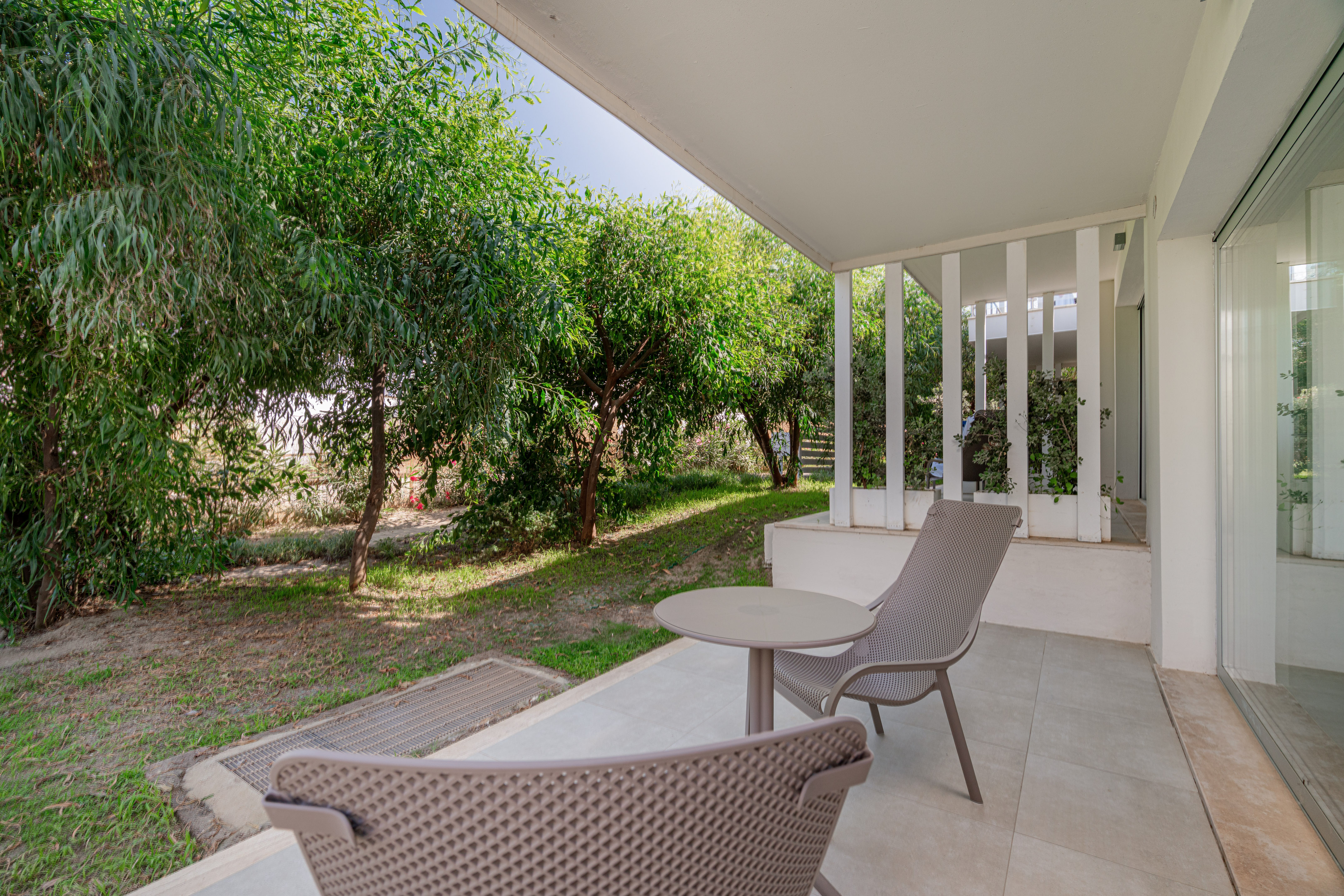 Tiled patio with outdoor seating, small table, and lush green garden view.