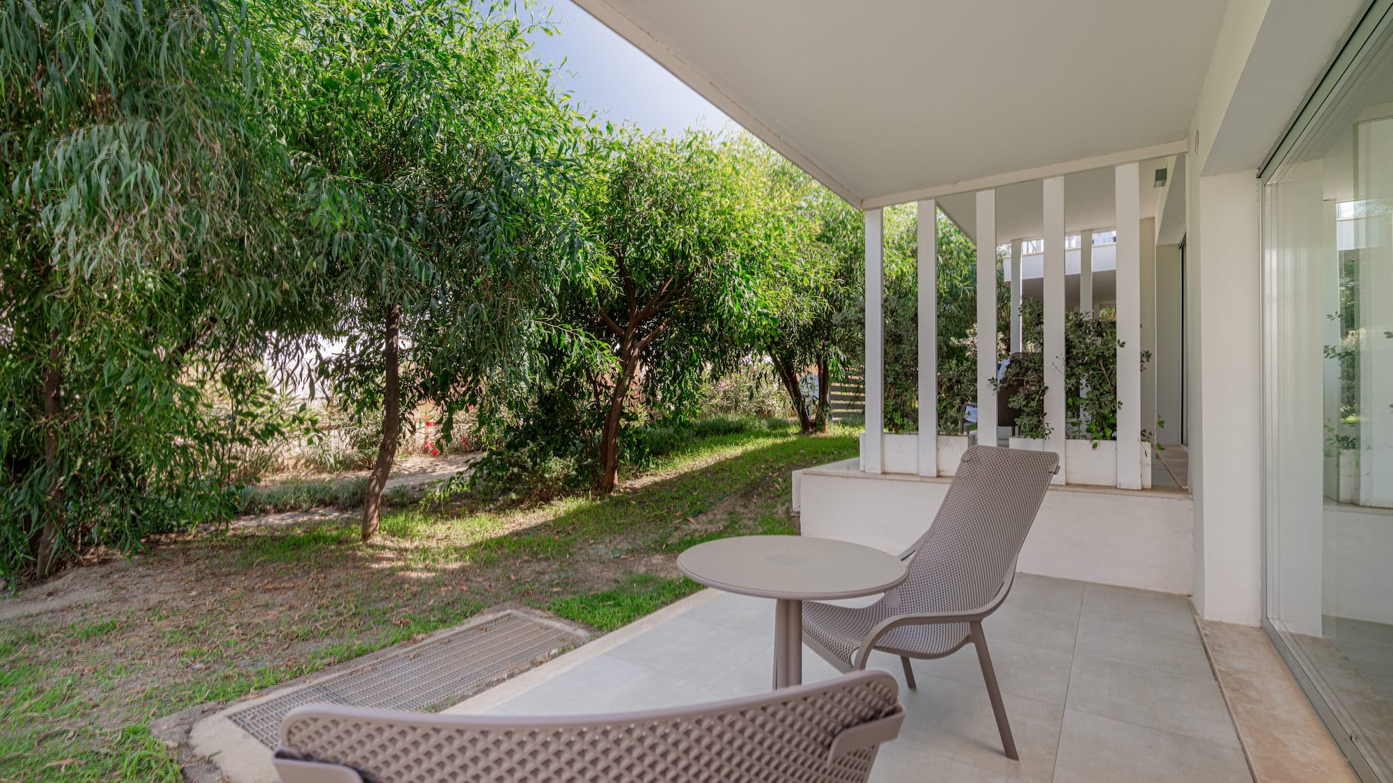 Tiled patio with outdoor seating, small table, and lush green garden view.