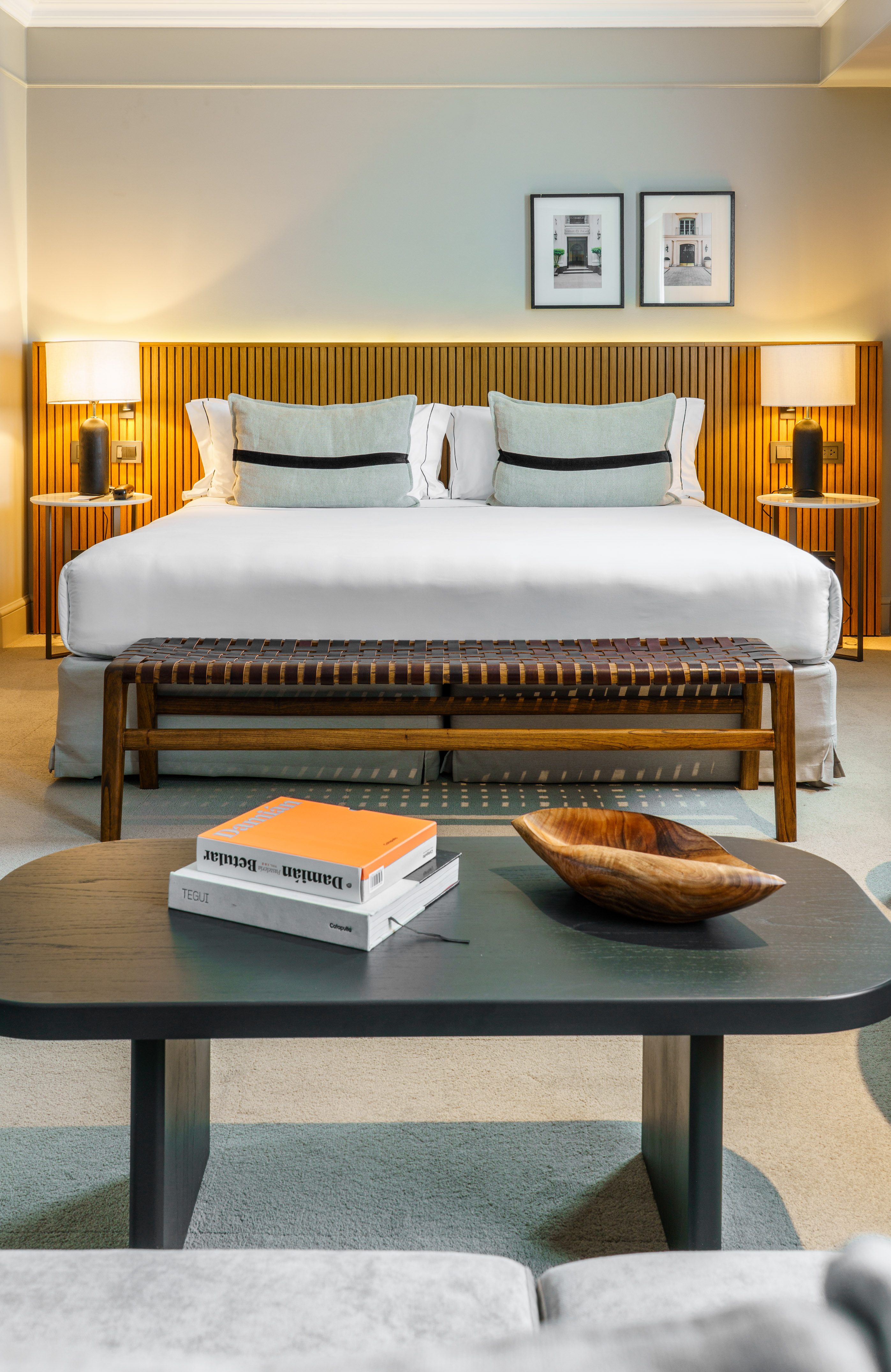 Modern hotel bedroom with wooden headboard, white bed, and woven bench.