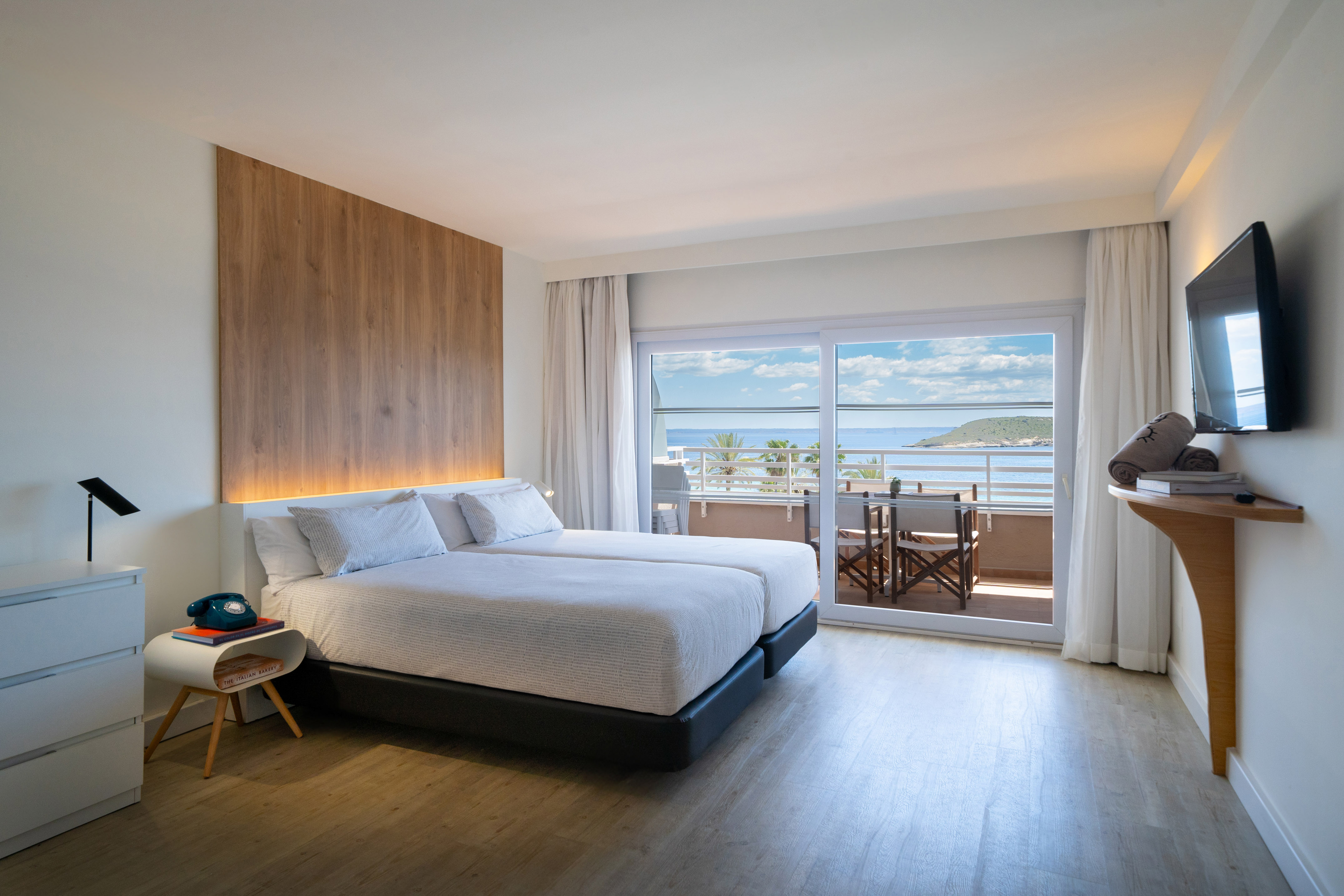 Modern hotel room with twin beds, wooden headboard, and ocean view balcony.