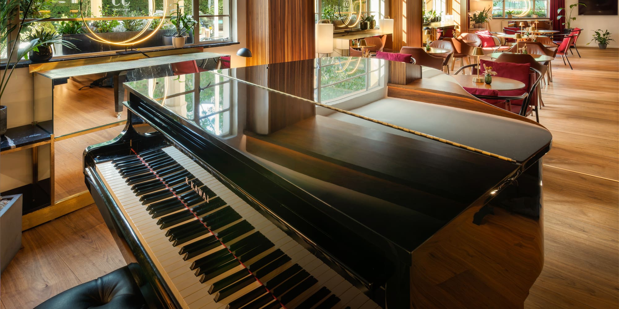 Elegant lounge with glossy grand piano, cafe seating, plants, and large windows.