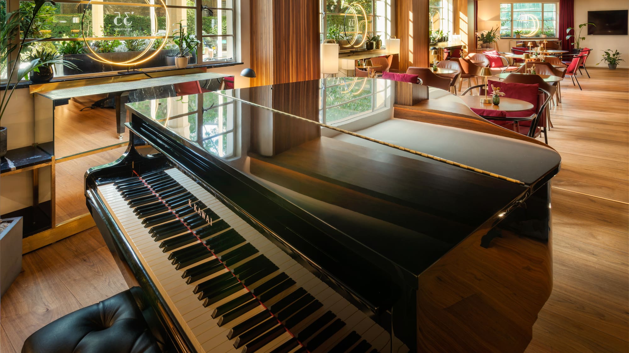 Elegant lounge with glossy grand piano, cafe seating, plants, and large windows.