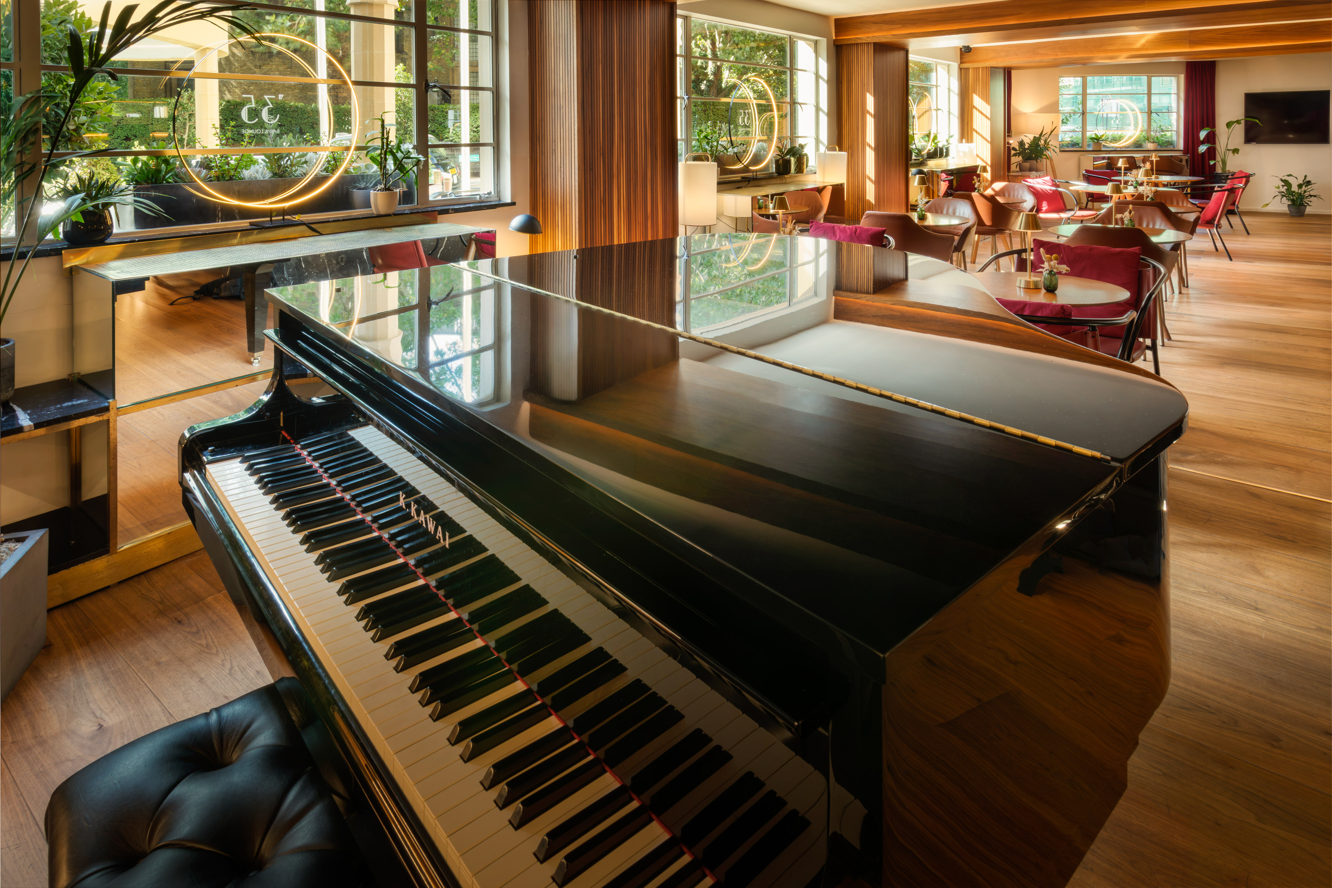 Elegant lounge with glossy grand piano, cafe seating, plants, and large windows.