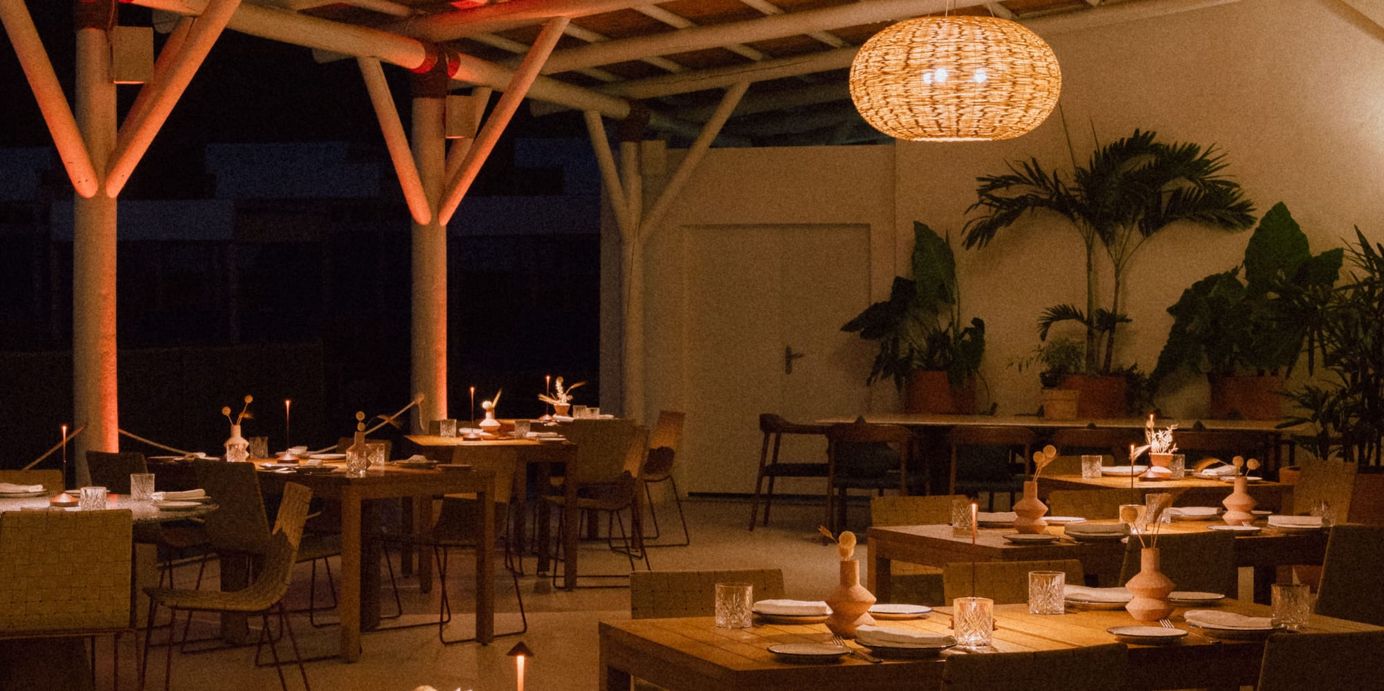 Warmly lit restaurant featuring bamboo ceiling, rattan lamps, and set tables.
