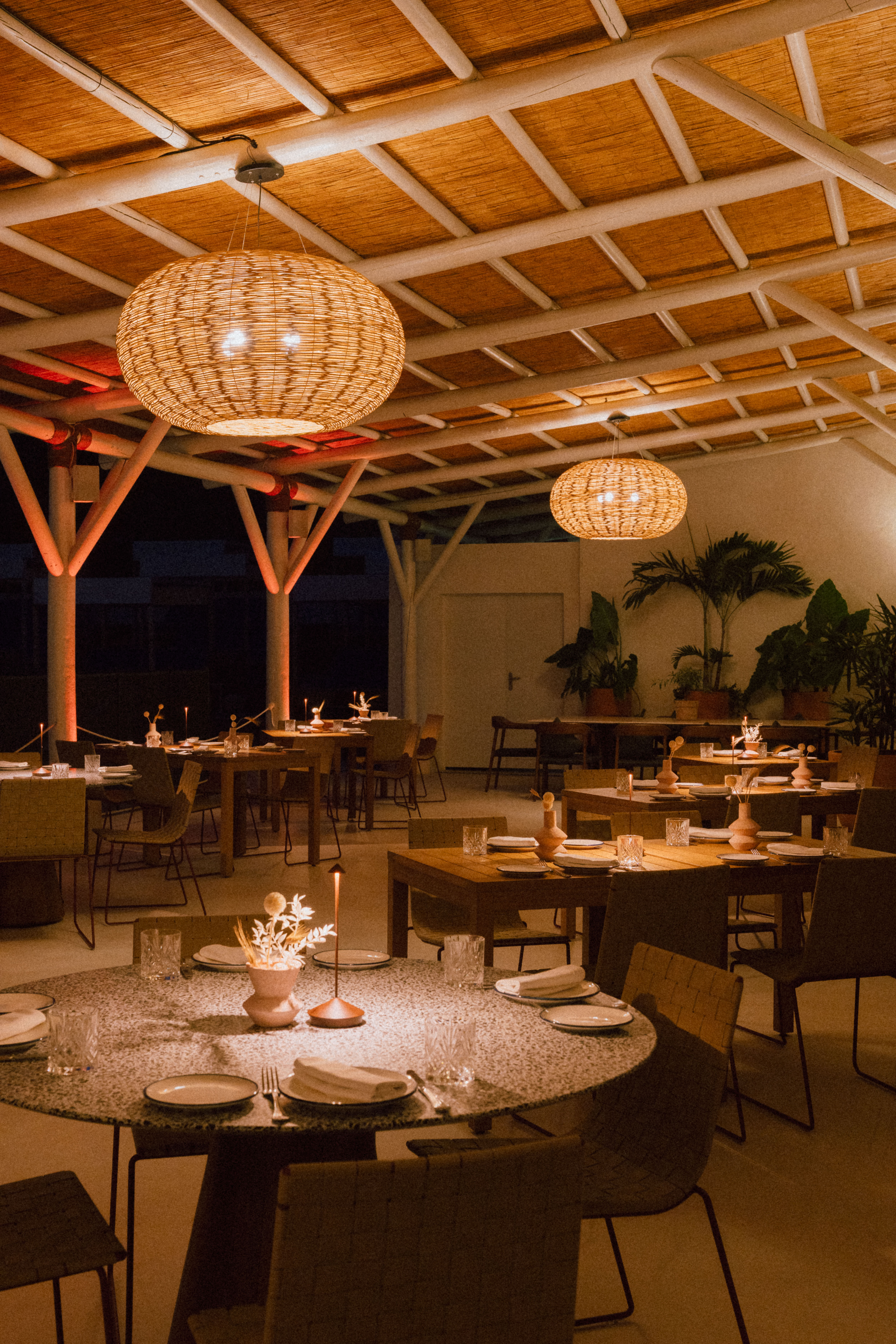 Warmly lit restaurant featuring bamboo ceiling, rattan lamps, and set tables.