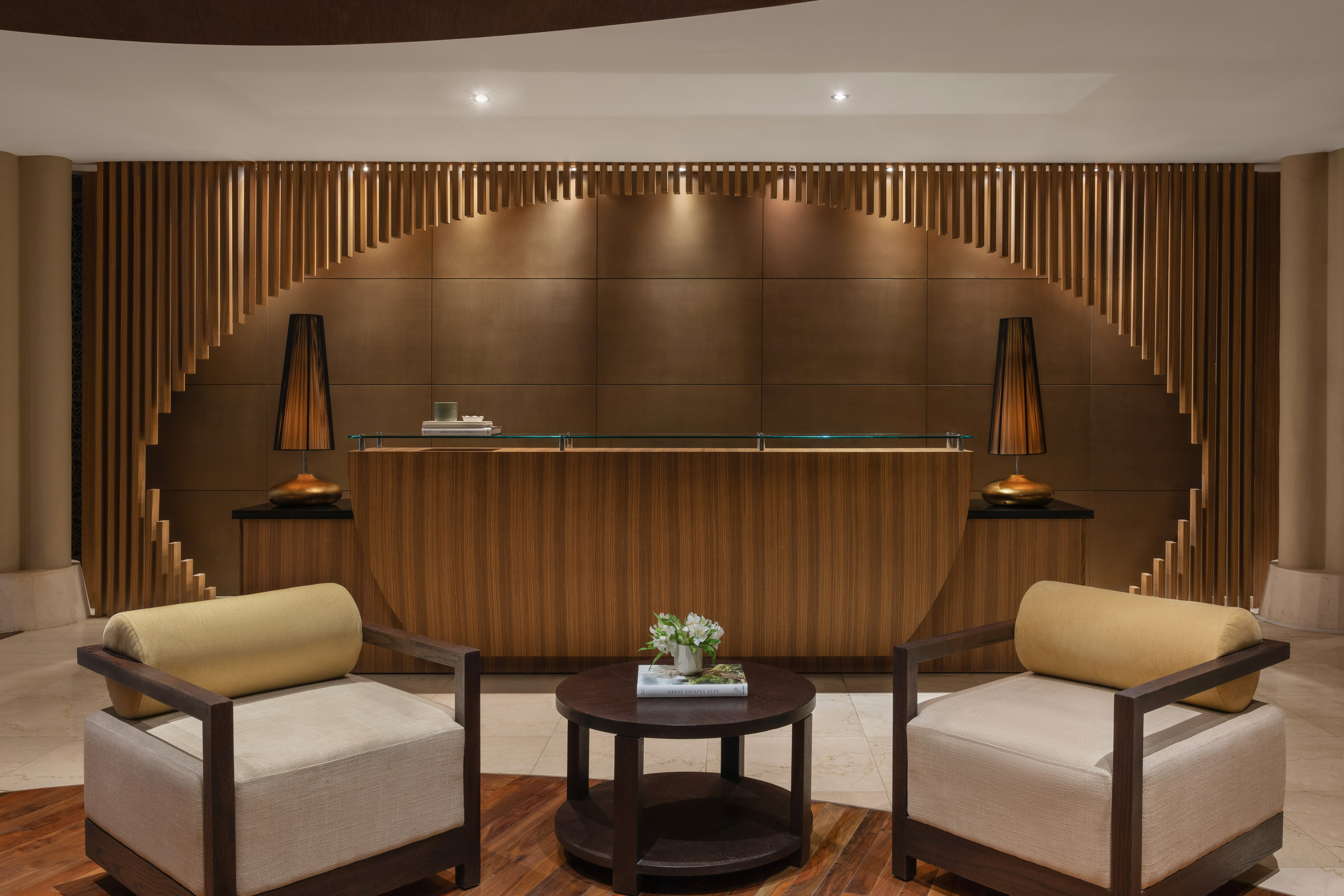 Modern hotel lobby featuring a wooden reception desk, slatted wall, and armchairs.