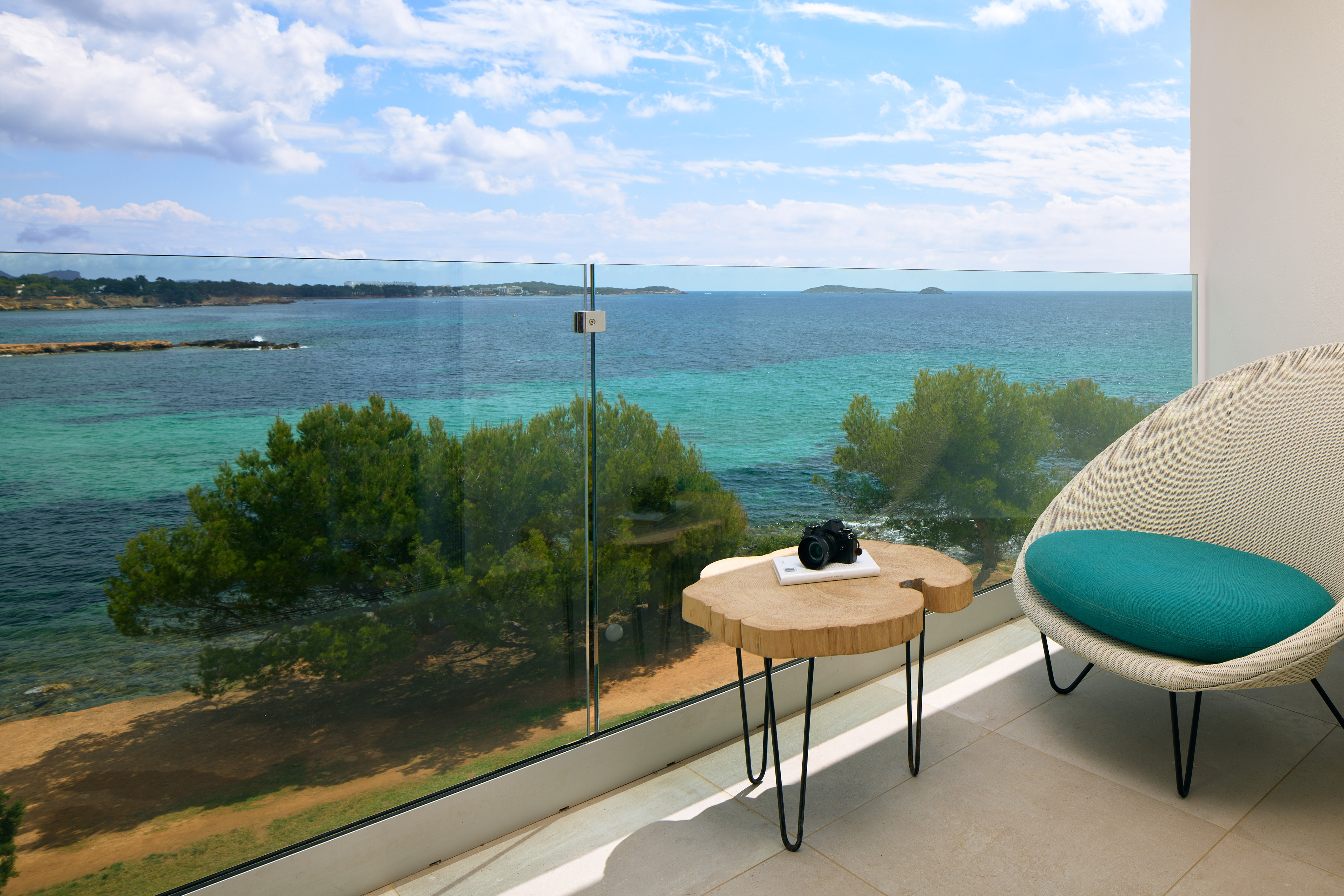Modern balcony with turquoise ocean view, glass railing, table, and armchair.