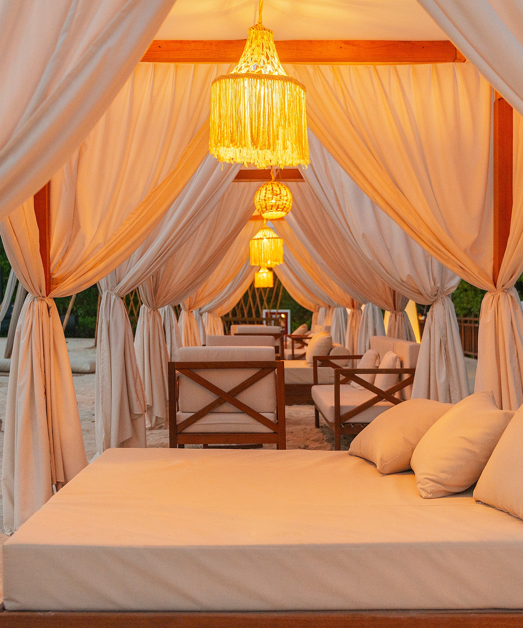 Tumbona de lujo en terraza balinesa con cortinas y luces cálidas al atardecer.