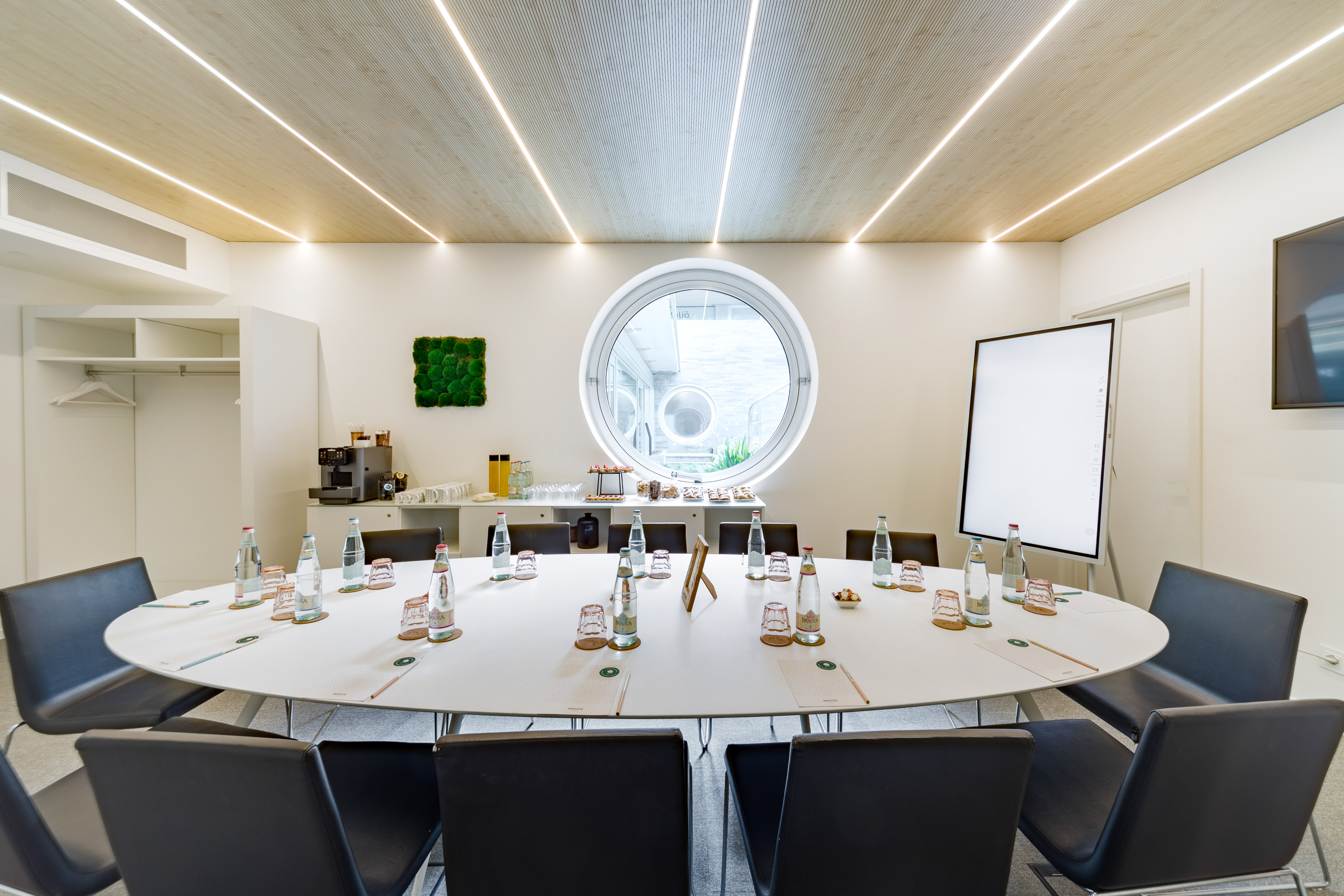 Modern meeting room with oval table, circular window, and refreshments.