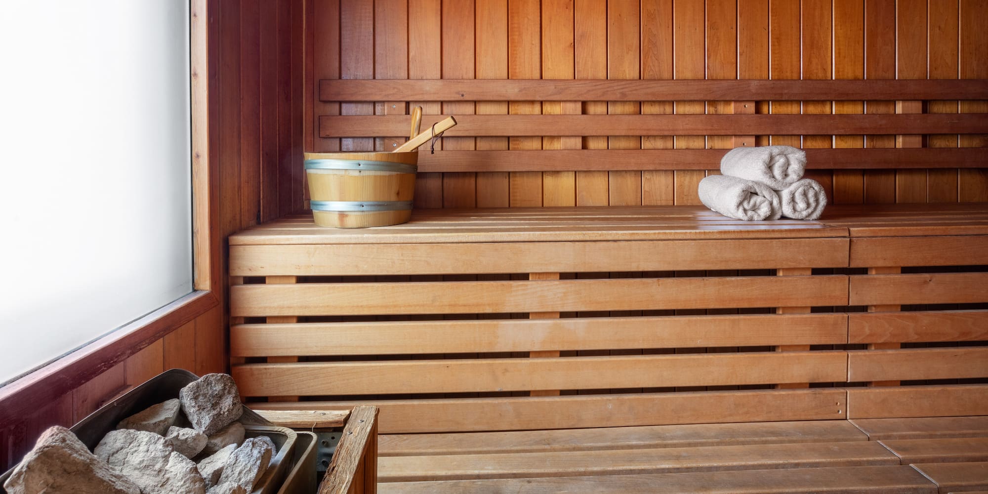 Cozy wooden sauna room with heater, water bucket, and rolled towels on benches.