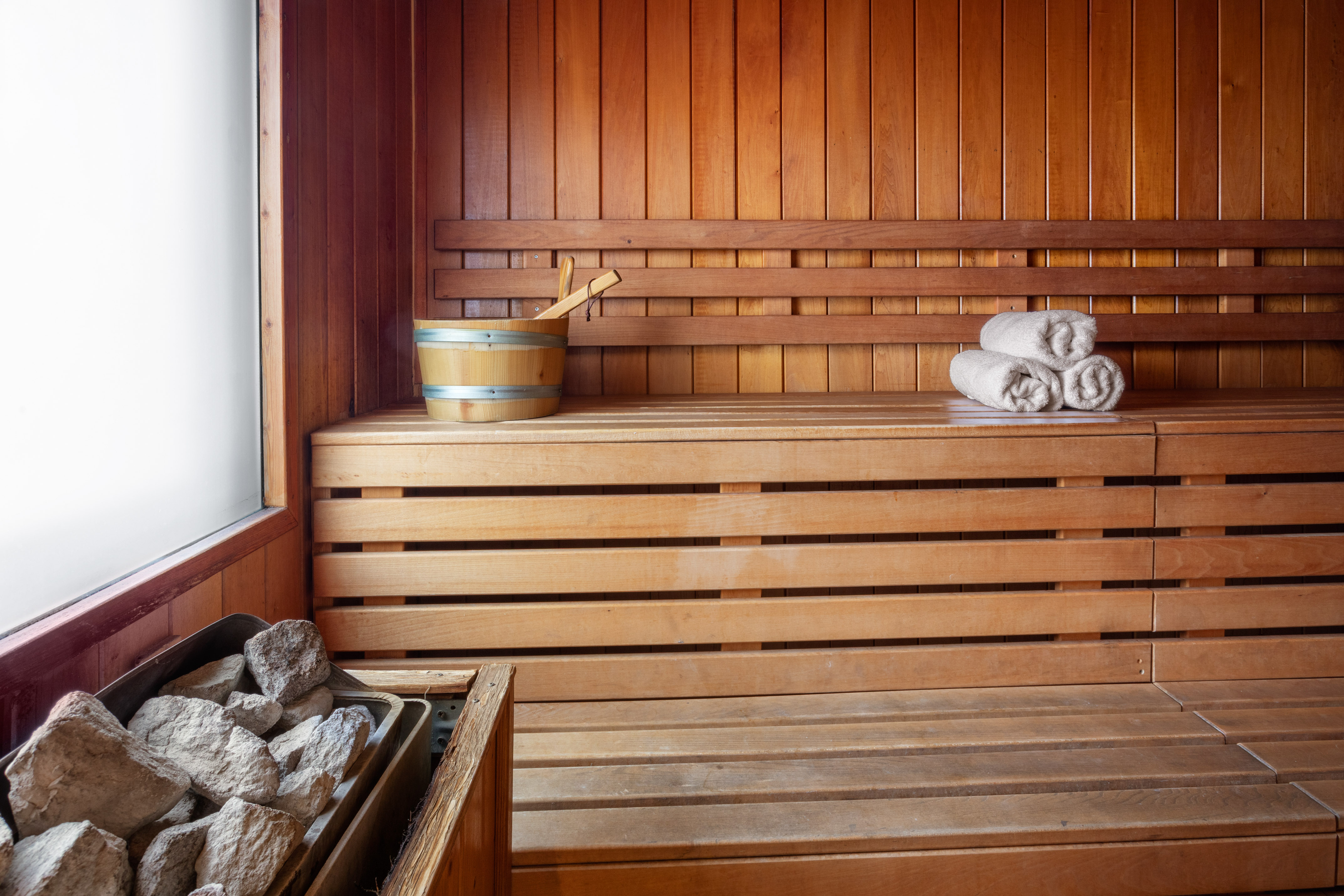 Cozy wooden sauna room with heater, water bucket, and rolled towels on benches.